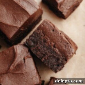 Rich Chocolate Brownies with Tangy Cream Cheese Frosting 12 Brownies covered in chocolate cream cheese frosting on parchment paper.