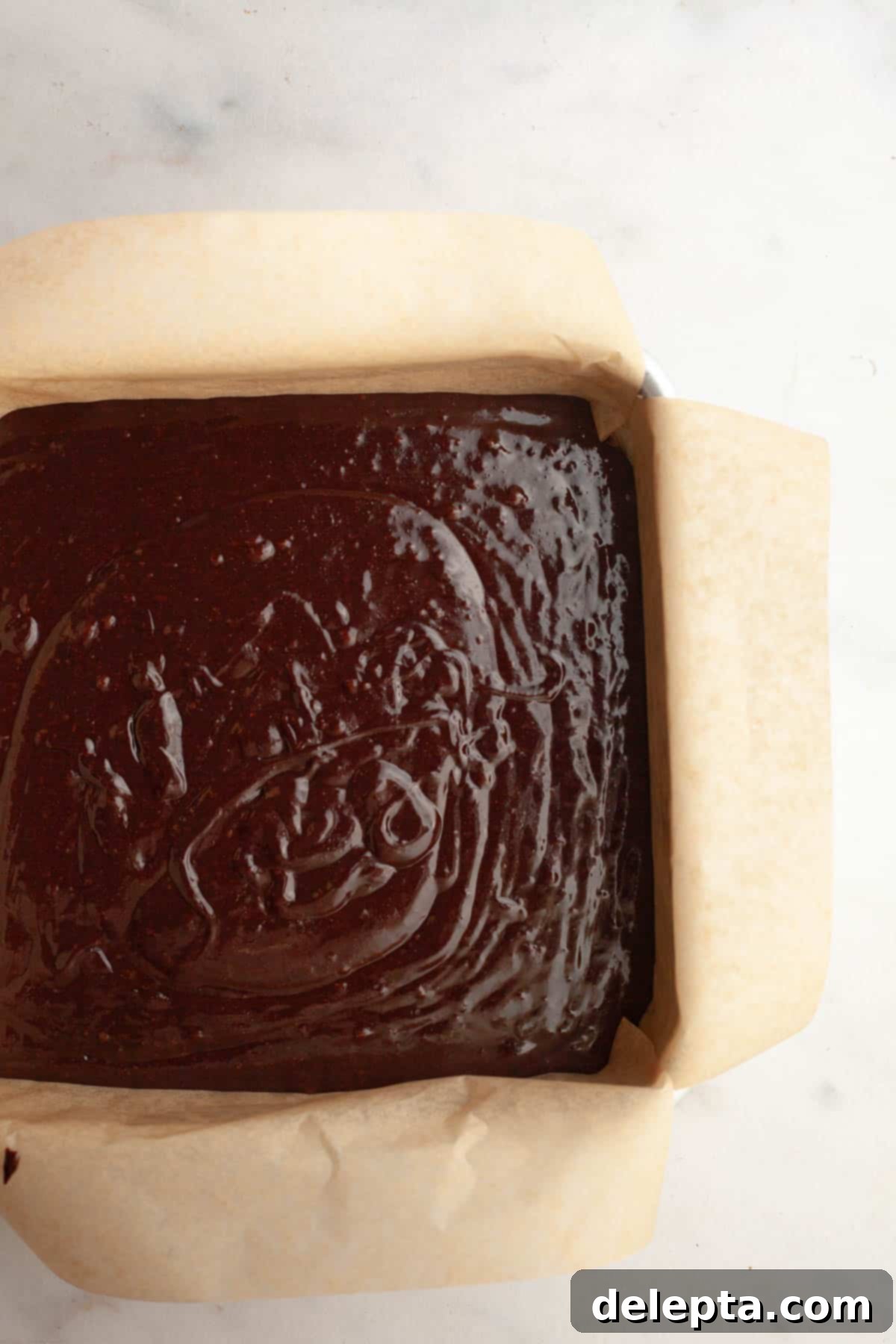 Rich Chocolate Brownies with Tangy Cream Cheese Frosting 7 Unbaked brownie batter in a parchment-lined square baking pan, ready for the oven.