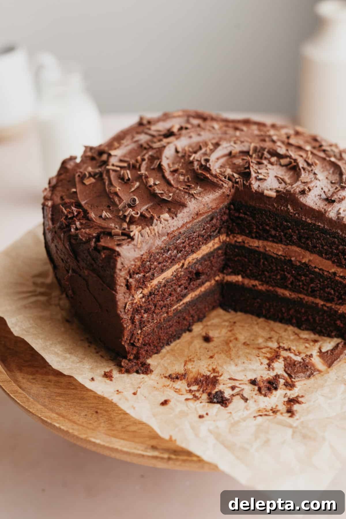 Ultimate Triple Chocolate Indulgence 2 A triple chocolate layer cake on parchment paper, several slices have been taken out, revealing its moist layers and rich filling.