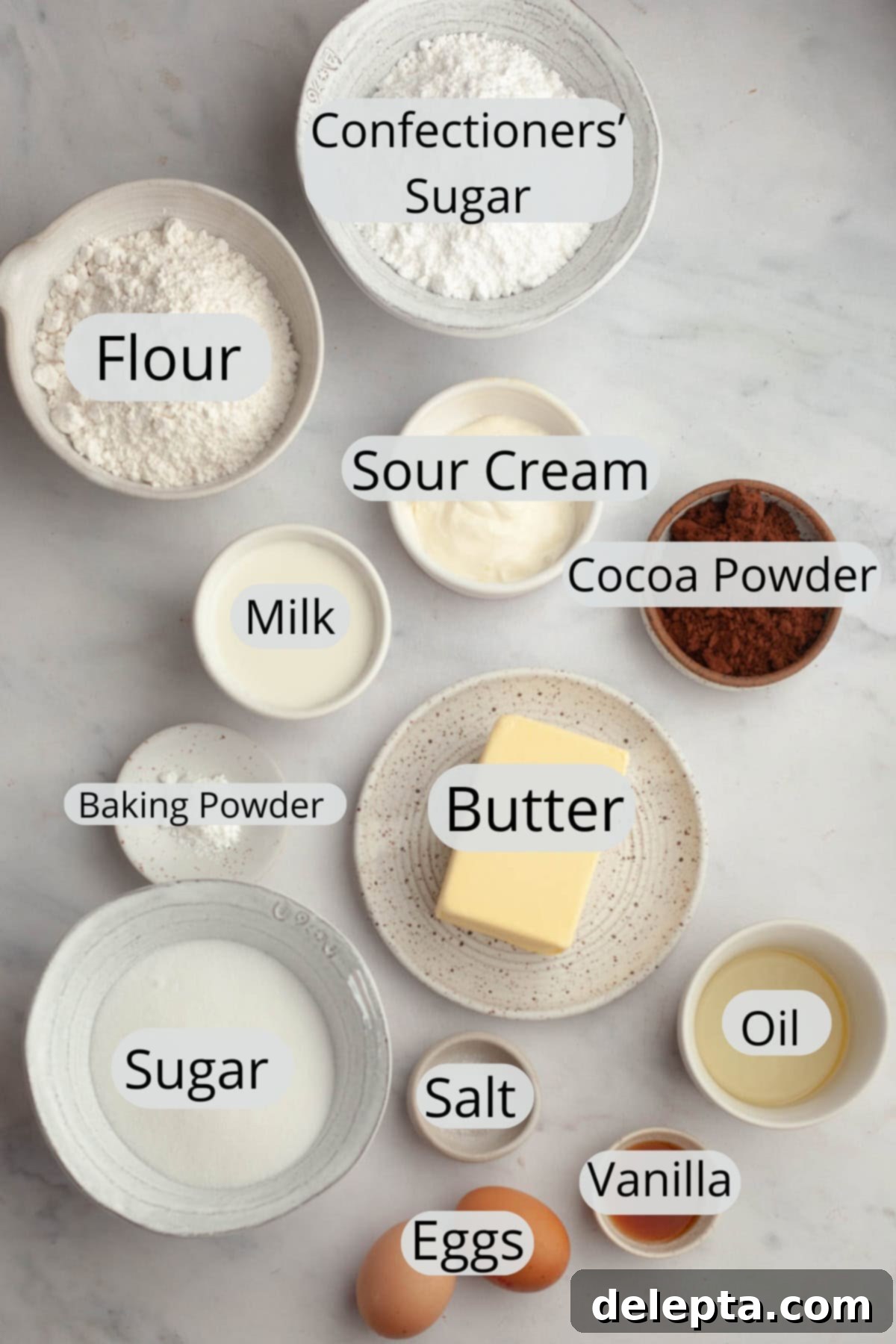 Velvety Vanilla, Chocolate Bliss 3 A collection of measured ingredients for vanilla cupcakes and chocolate frosting, neatly arranged in small white bowls on a pristine marble surface, ready for baking.