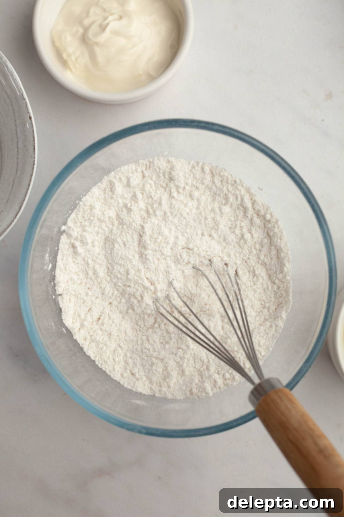 Velvety Vanilla, Chocolate Bliss 4 A small, pristine white bowl filled with cake flour, accompanied by a silver whisk, indicating the initial preparation step for dry ingredients.
