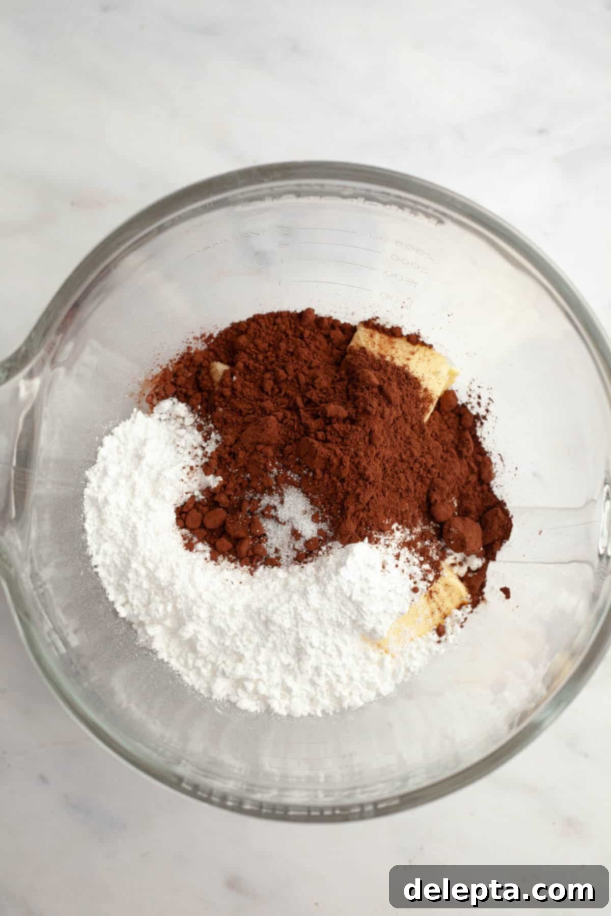 Velvety Vanilla, Chocolate Bliss 8 A large mixing bowl containing softened butter, confectioners' sugar, and rich Dutch-processed cocoa powder, ready to be beaten into creamy chocolate frosting.