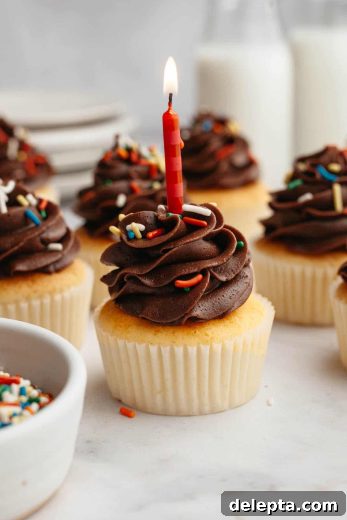 Velvety Vanilla, Chocolate Bliss 10 A beautifully frosted vanilla cupcake with rich chocolate buttercream, adorned with a single white birthday candle, ready for a celebration.