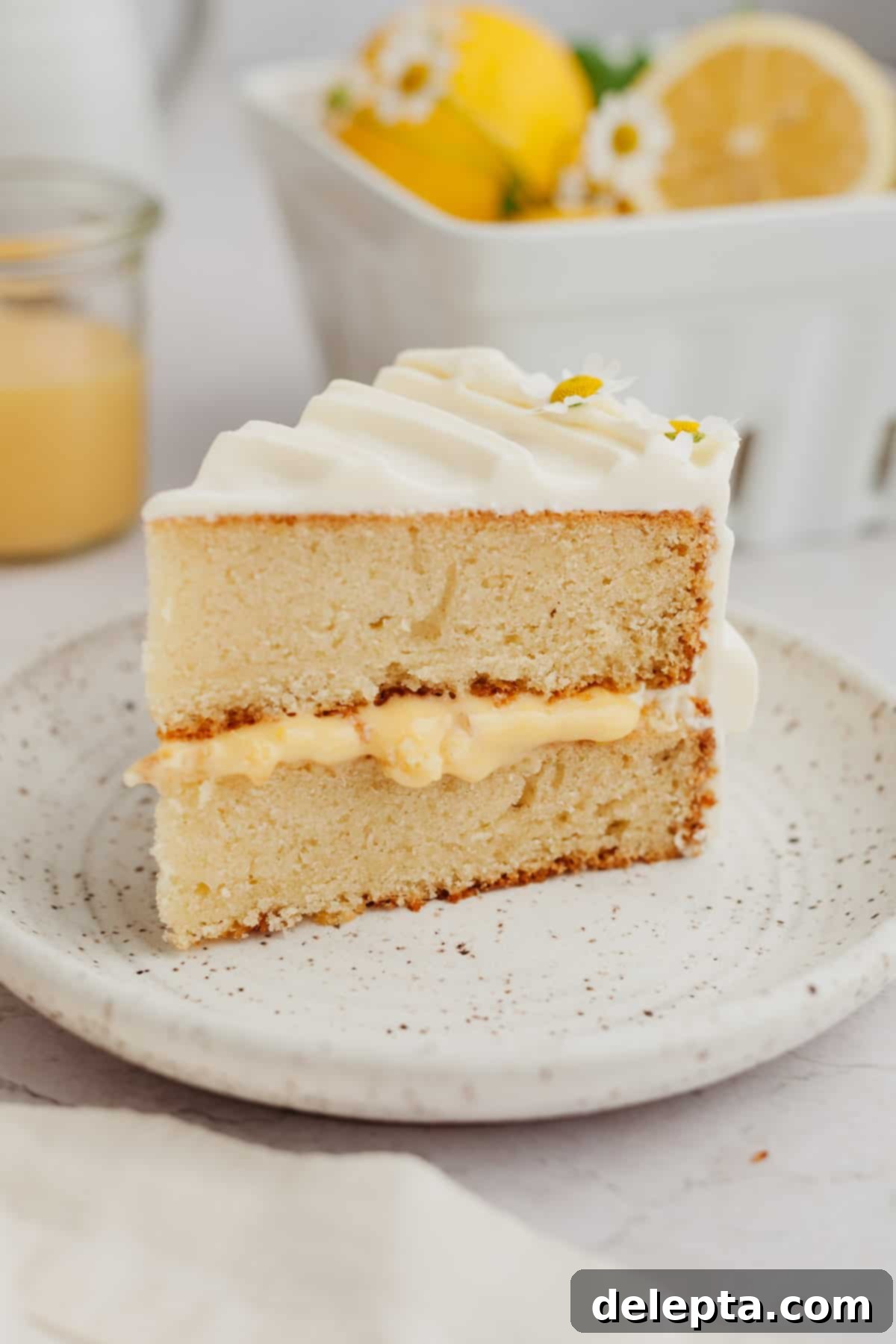 Zesty Lemon Curd Delight 2 A perfectly sliced piece of homemade lemon curd cake adorned with a lemon slice and a berry on a white plate, showcasing its moist layers and creamy filling.