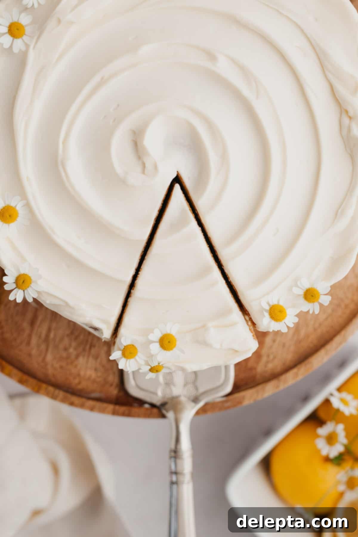 Zesty Lemon Curd Delight 11 A beautifully decorated lemon curd cake on a cake stand, garnished with delicate daisies. A single slice has been removed, revealing the delicious layers.