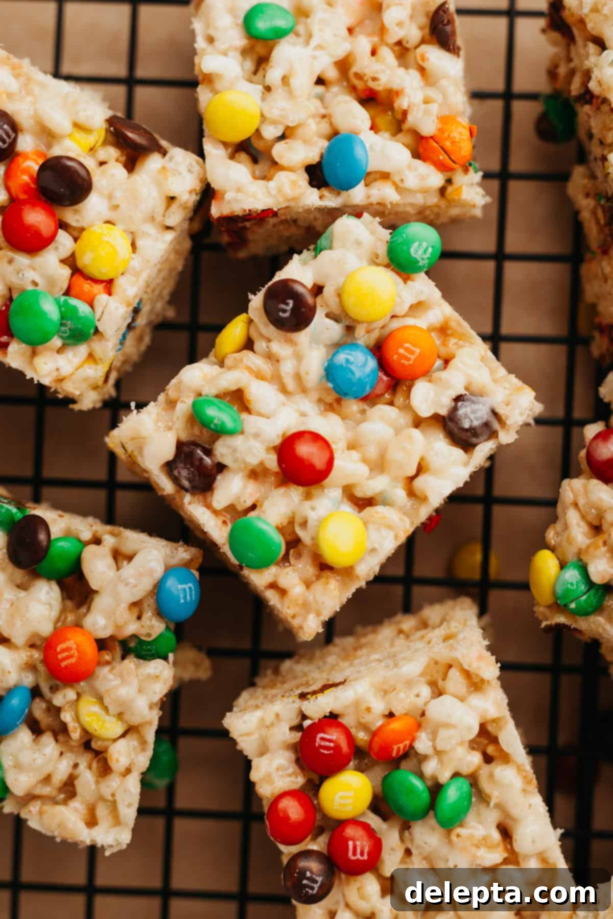 Colorful M and M Krispie Bars 6 A top-down shot of several M&M Rice Krispie treats, some whole and some cut, scattered on parchment paper.