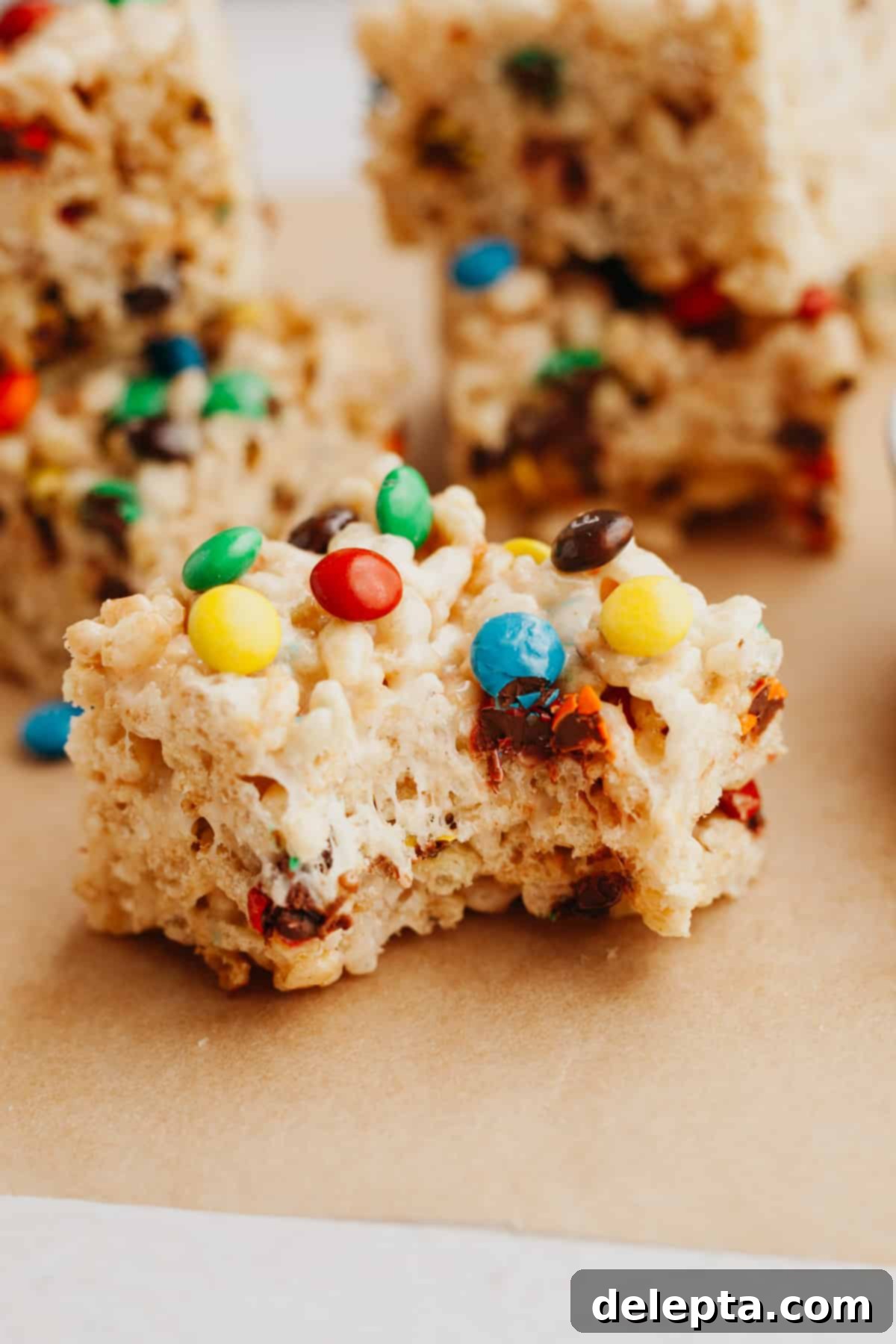 Colorful M and M Krispie Bars 7 A close-up shot of an M&M Rice Krispie treat with a bite taken out, revealing its gooey interior and colorful candies.