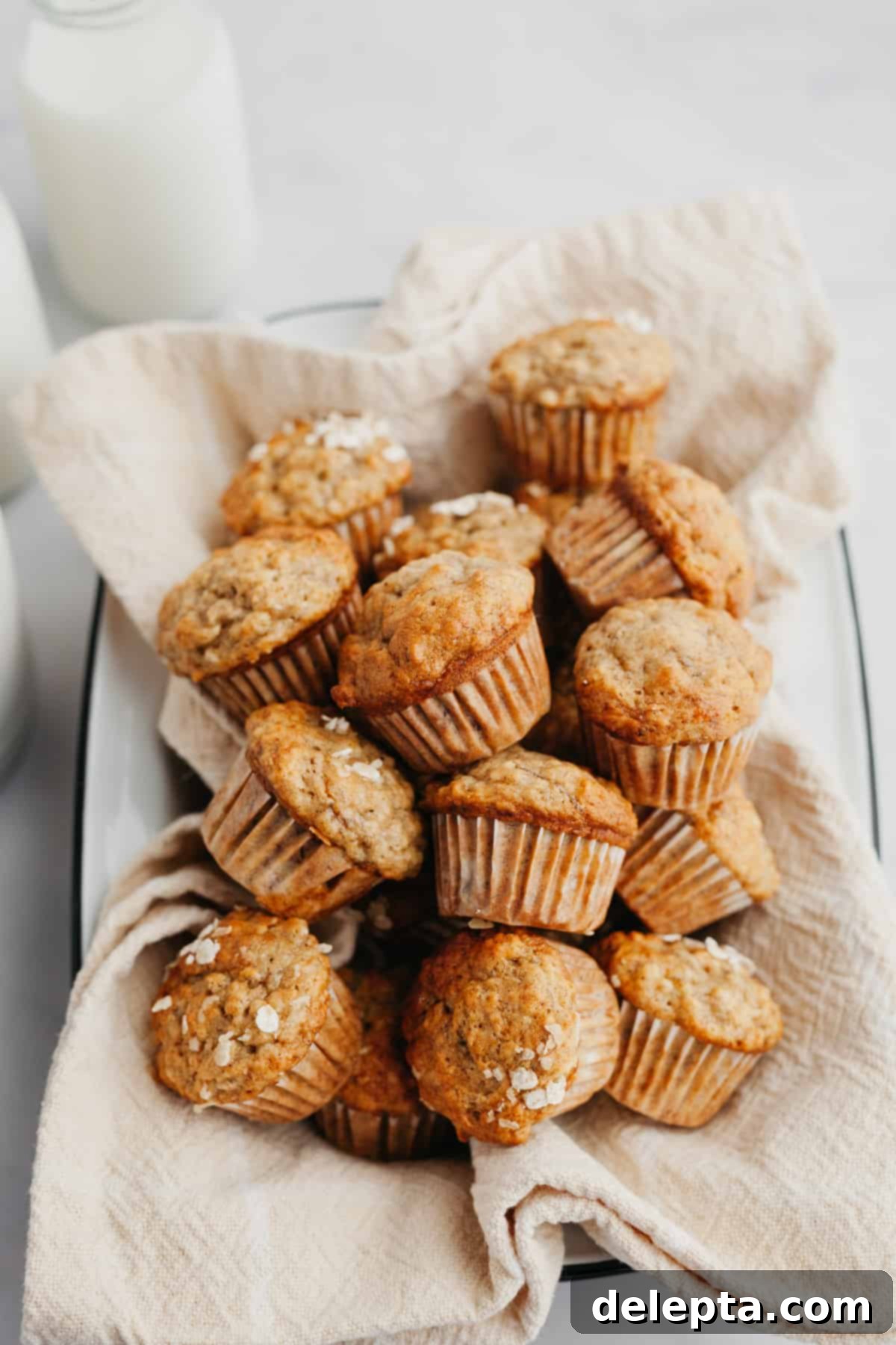 Golden Banana Bites 6 A charming metal tin lined with a beige linen, generously filled with an abundance of freshly baked banana mini muffins, ready to be enjoyed.