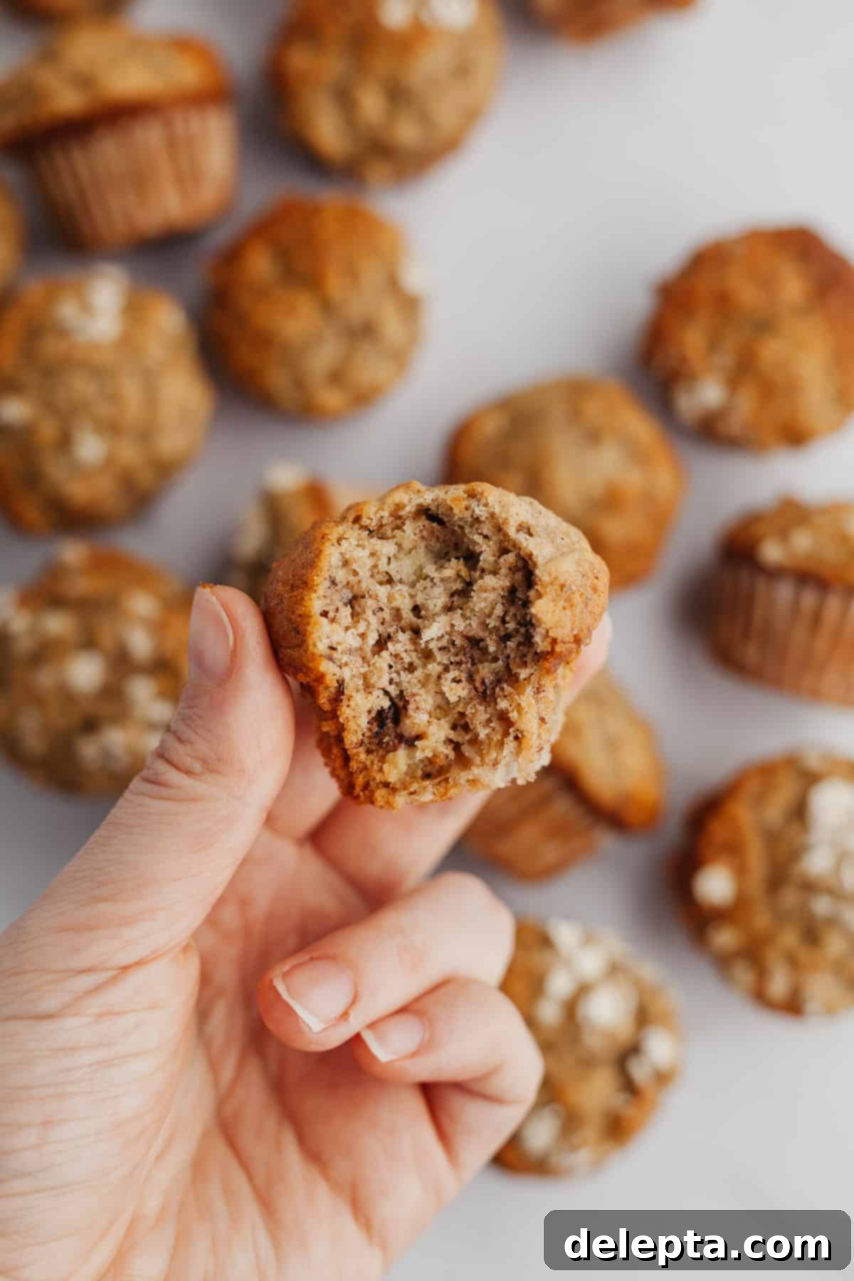 Golden Banana Bites 7 A hand holding a perfectly baked banana mini muffin, showing its soft, fluffy interior with a bite taken out.