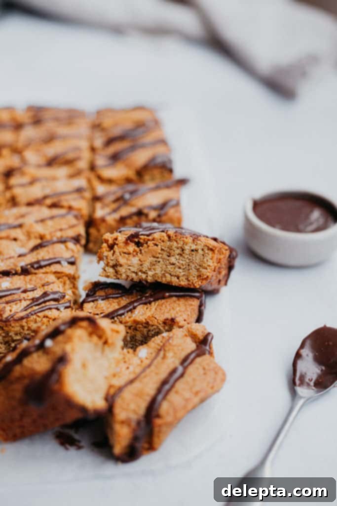 Java Peanut Butter Crunch Blondies 3 A side view of a coffee blondie, next to a spoon and small pot of mocha drizzle