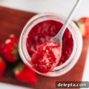 Easy 3 Ingredient Strawberry Cake Filling 7 A mason jar with homemade strawberry filling for cake, featuring a silver spoon.