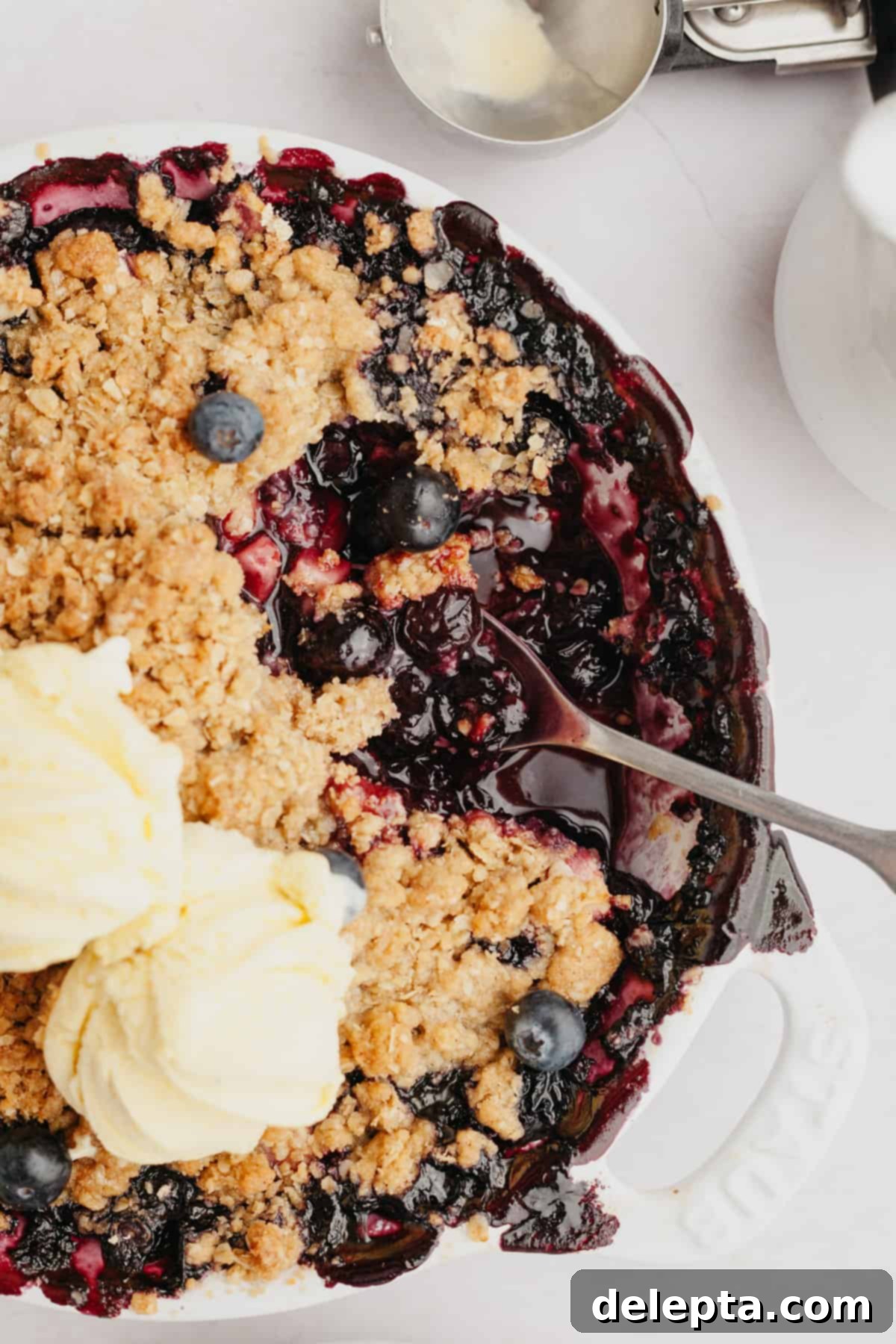 Golden Apple and Berry Crumble 2 A warm blueberry apple crumble topped with two scoops of creamy vanilla ice cream, perfectly golden and ready to be enjoyed with a spoon.