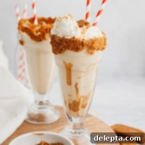 Creamy Biscoff Milkshake 6 Two biscoff milkshakes in large glasses with red and white straws, topped with whipped cream and crushed cookies.