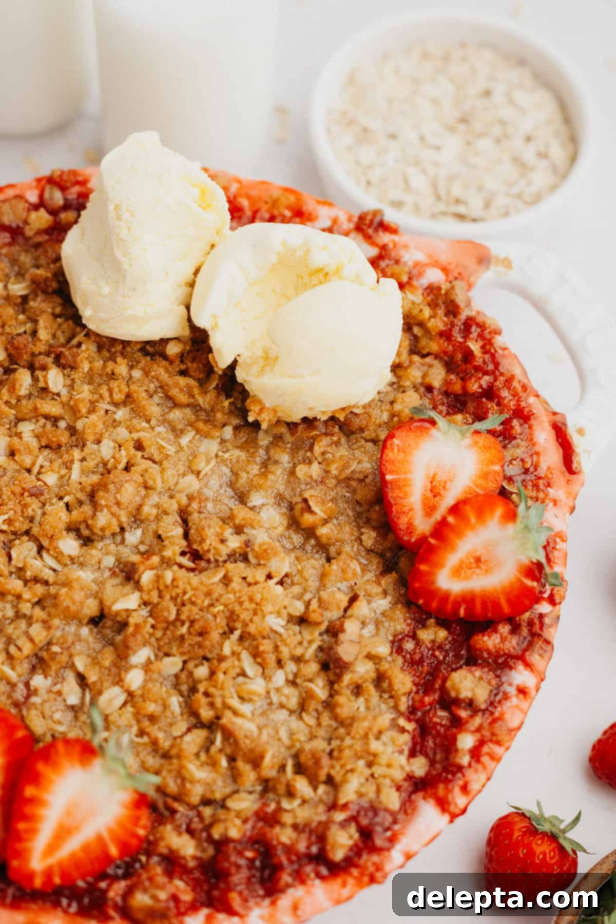 Strawberry Sunshine Crumble 2 A beautifully baked strawberry crumble in a white ceramic dish, garnished with fresh sliced strawberries and two generous scoops of vanilla ice cream melting on top.