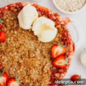 Strawberry Sunshine Crumble 8 A warm strawberry crumble in a white dish, topped with fresh sliced strawberries and two scoops of creamy vanilla ice cream.