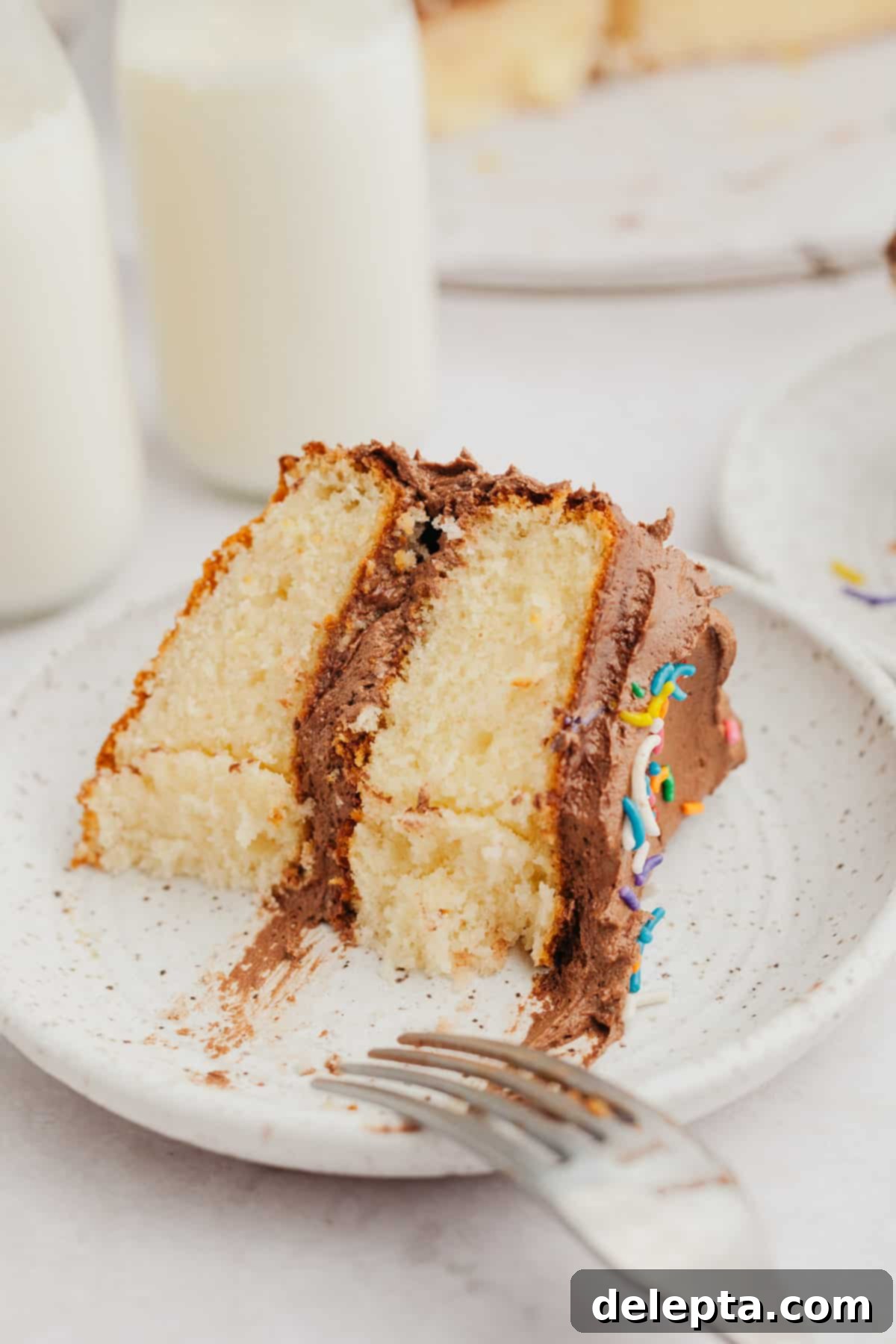 Golden Vanilla Treat with Chocolate Bliss 10 A tempting slice of vanilla cake with a thick layer of rich chocolate frosting, ready to be enjoyed.