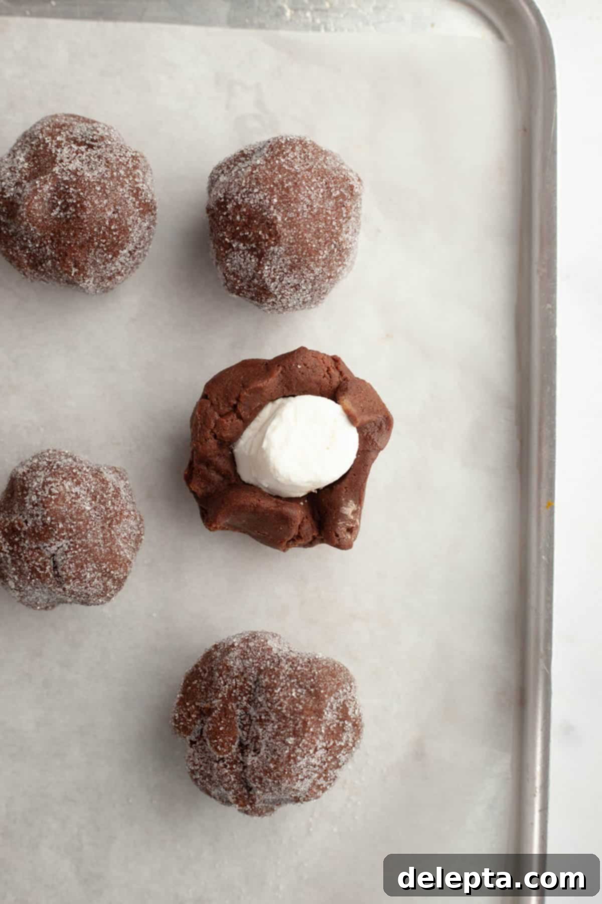 Gooey Chocolate Marshmallow Cookies 7 Chocolate cookie dough balls, some rolled in sugar, with one showing a marshmallow peeking out.