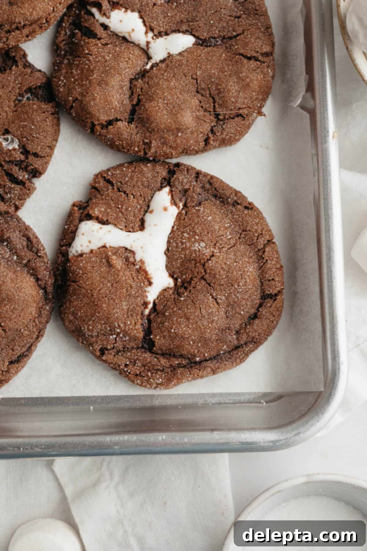 Gooey Chocolate Marshmallow Cookies 9 Freshly baked chocolate marshmallow cookies with slightly melted, gooey centers on parchment paper.