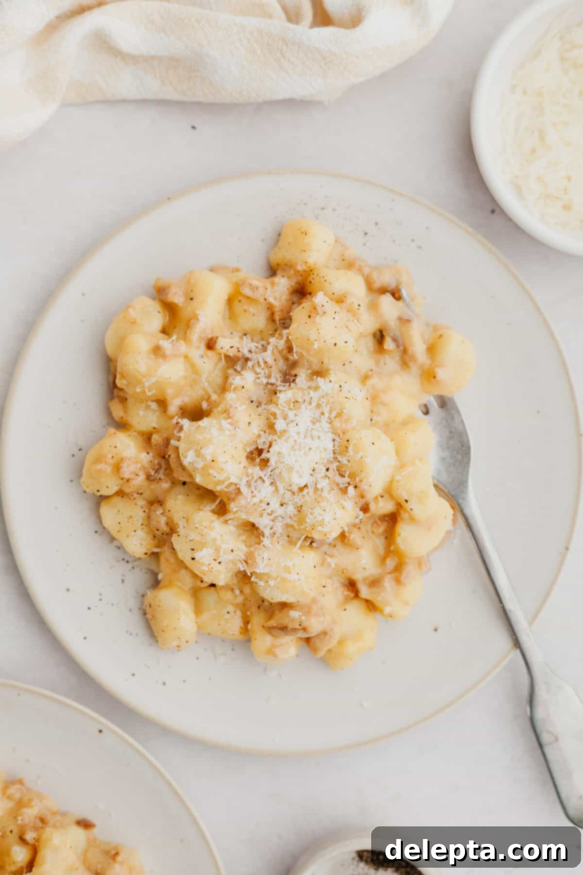 Classic Gnocchi Carbonara 2 Gnocchi carbonara on a white plate, garnished with fresh black pepper and grated cheese.