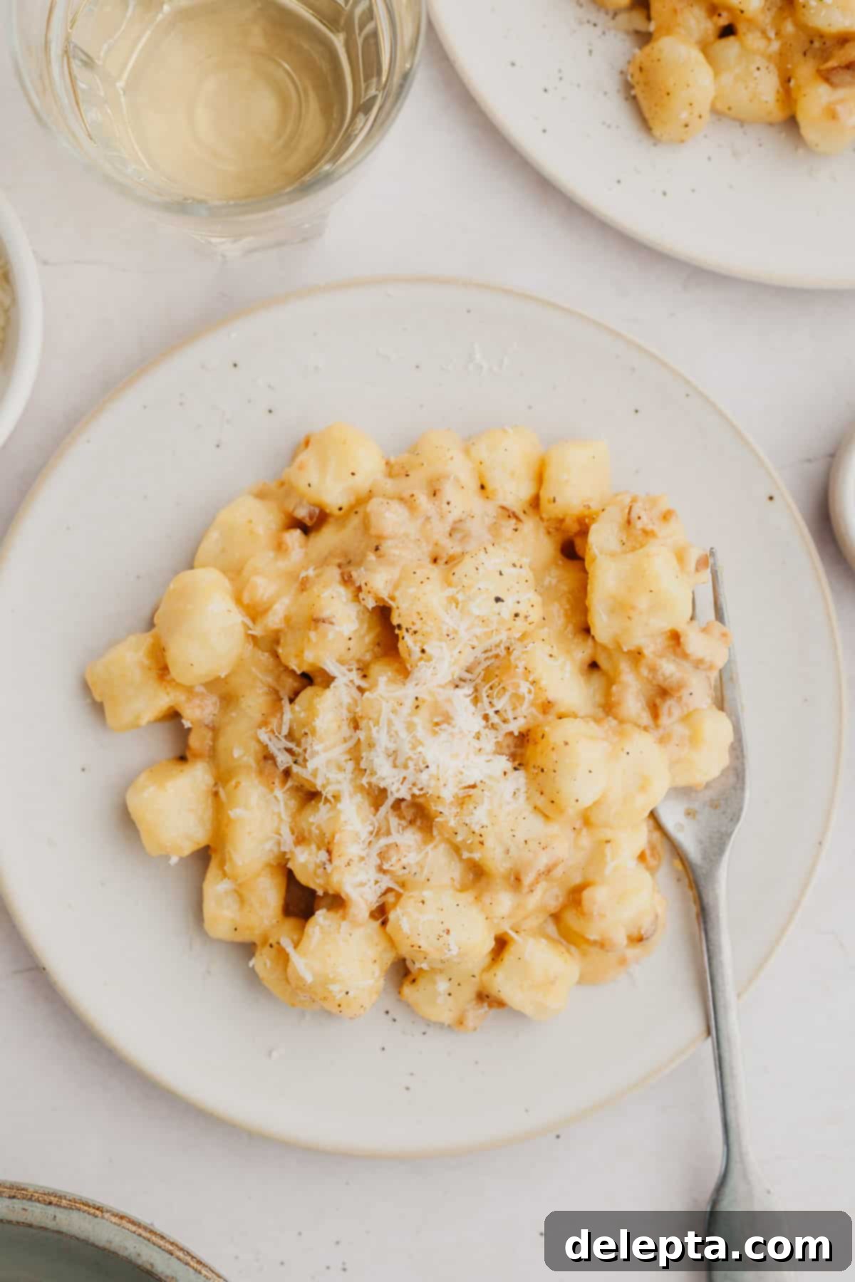 Classic Gnocchi Carbonara 7 A close-up of a plate of gnocchi carbonara, topped with fresh black pepper and grated cheese.