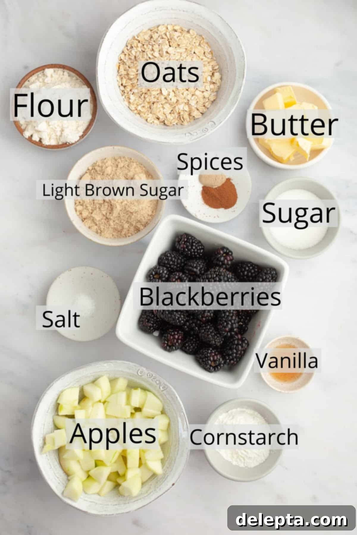 Golden Apple and Blackberry Crumble 3 All the pre-measured ingredients for blackberry apple crumble laid out in small bowls, including fresh fruit, flour, oats, sugar, and butter.
