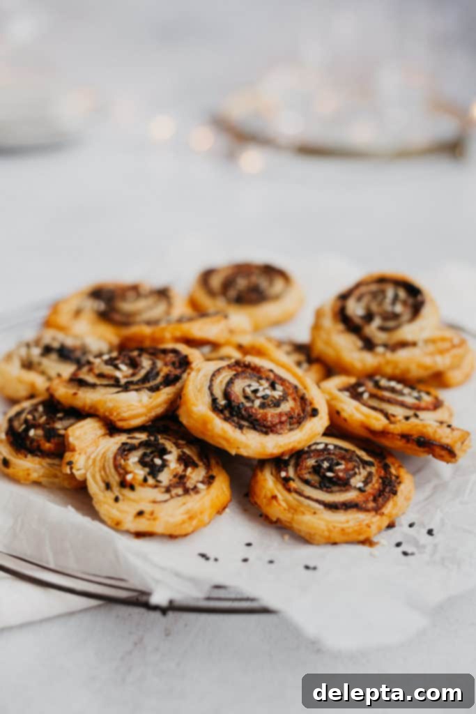 Golden Tapenade Spirals 3 a pile of sesame and tapenade pinwheels on some parchment paper, fairy lights behind