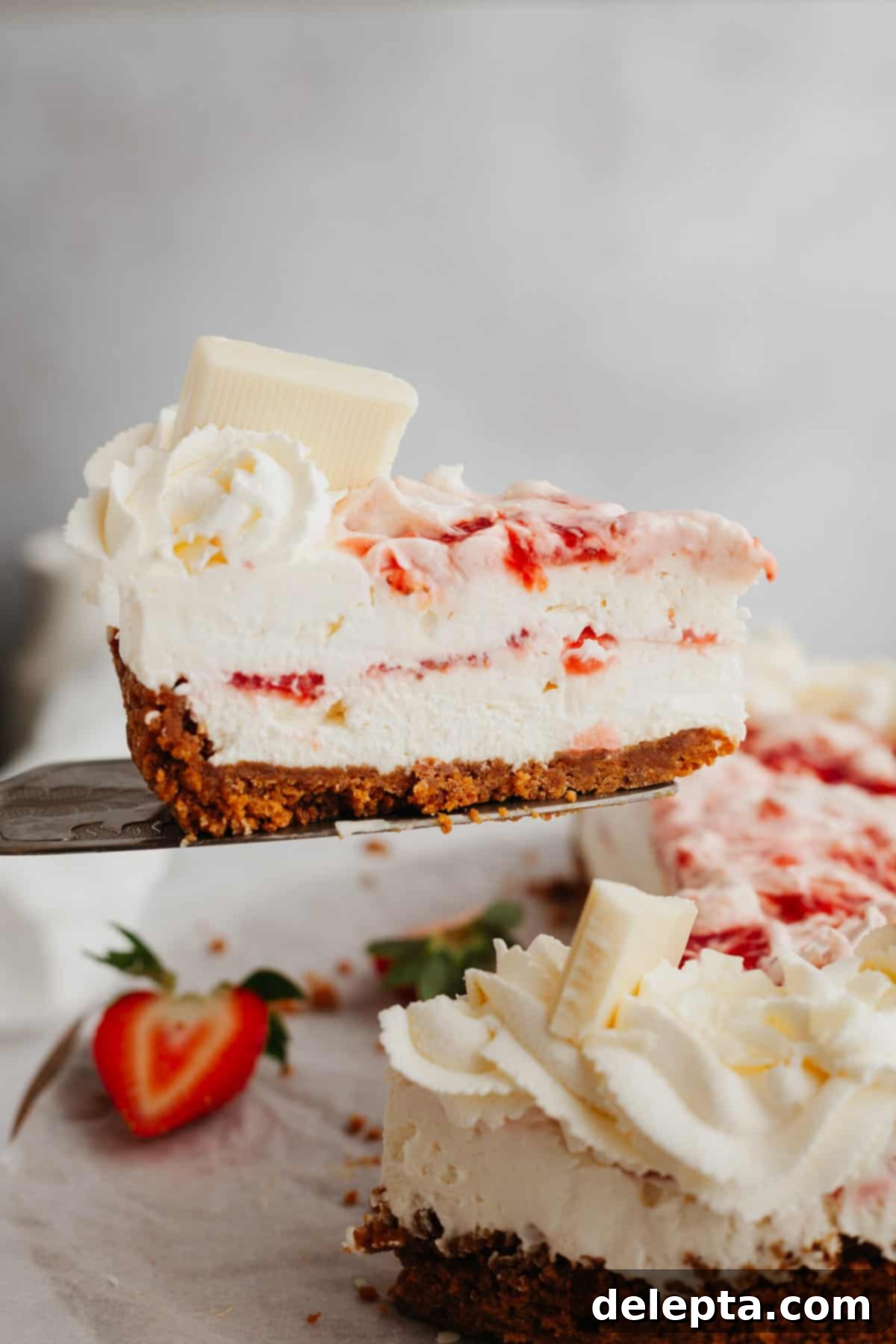 Effortless No Bake Strawberry White Chocolate Cheesecake 7 A beautiful slice of strawberry and white chocolate cheesecake being carefully lifted with a cake server, ready to be enjoyed.