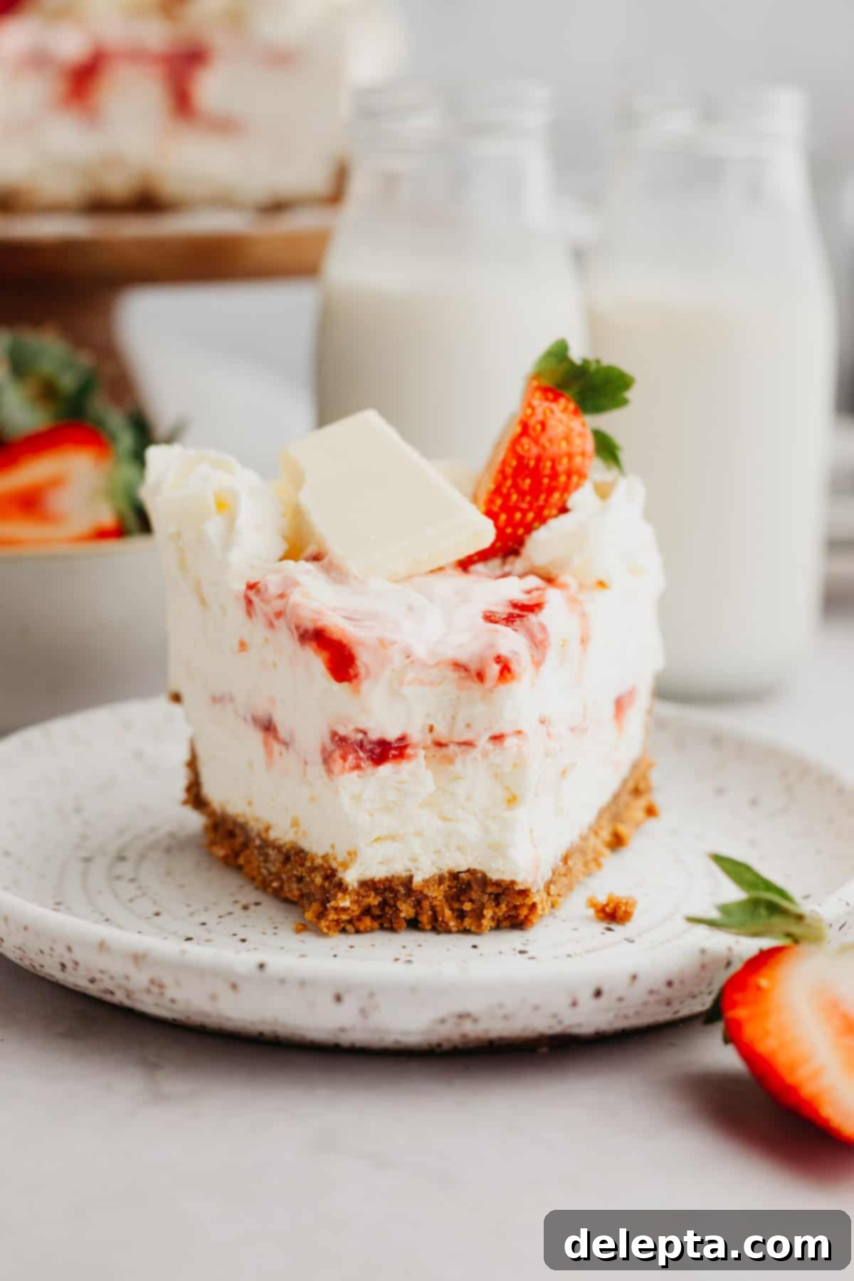 Effortless No Bake Strawberry White Chocolate Cheesecake 8 A beautifully presented white chocolate strawberry cheesecake on a pristine white plate, garnished with fresh fruit.