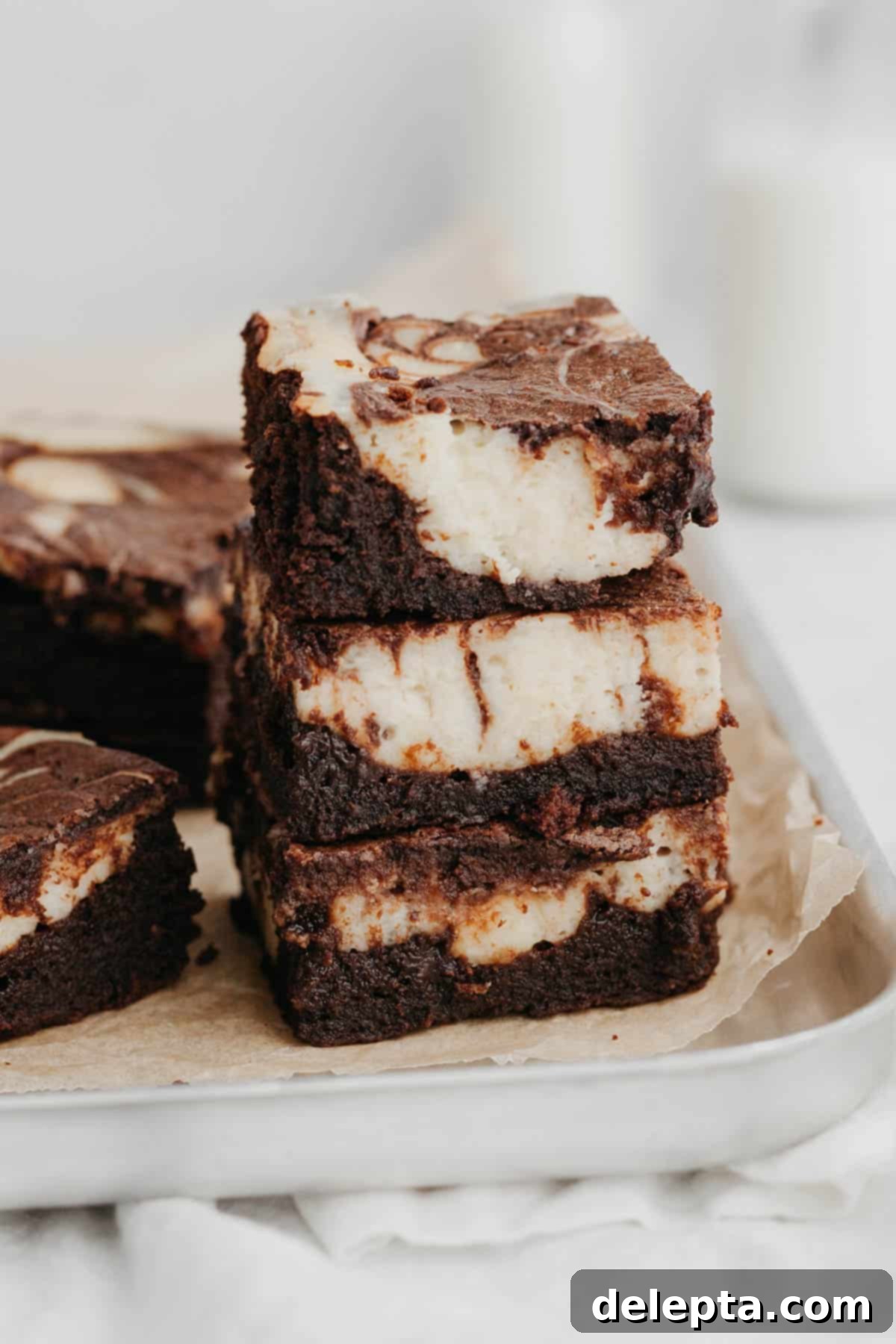 Decadent Cheesecake Brownie Swirls 2 A stack of three rich, fudgy marbled cheesecake brownies, showcasing the distinct swirl of chocolate and cream cheese, presented on a sleek silver baking tray.