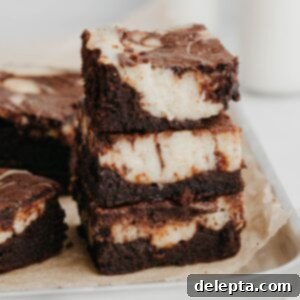 Decadent Cheesecake Brownie Swirls 11 A stack of three cheesecake brownies on a silver baking tray, highlighting the swirled cream cheese topping.