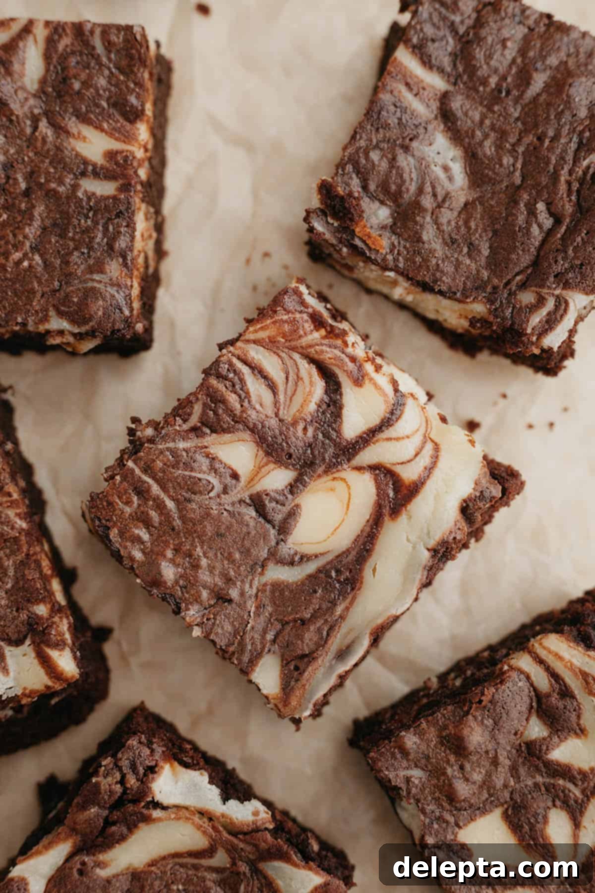 Decadent Cheesecake Brownie Swirls 9 A close-up view of several perfectly baked marbled cream cheese brownies, displaying their rich chocolate base and creamy, swirled topping, resting on light brown parchment paper.