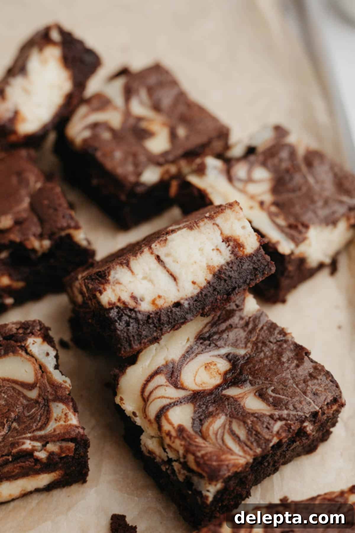 Decadent Cheesecake Brownie Swirls 10 An enticing arrangement of several marbled cream cheese brownies on light brown parchment paper, highlighting their perfect texture and delicious swirl.