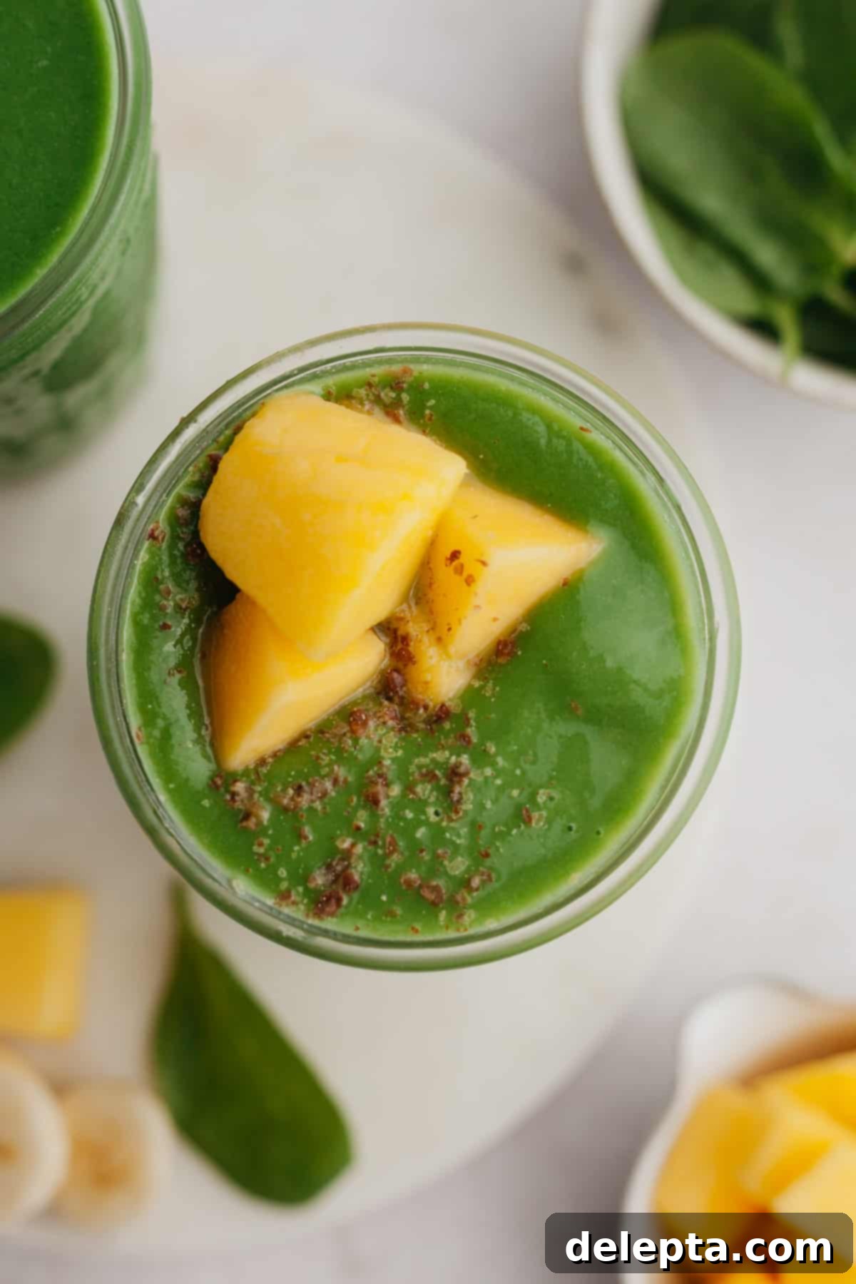 Vibrant Mango Spinach Smoothie 5 An inviting overhead shot of a luscious green smoothie in a glass, garnished with fresh mango cubes and a sprinkle of seeds.