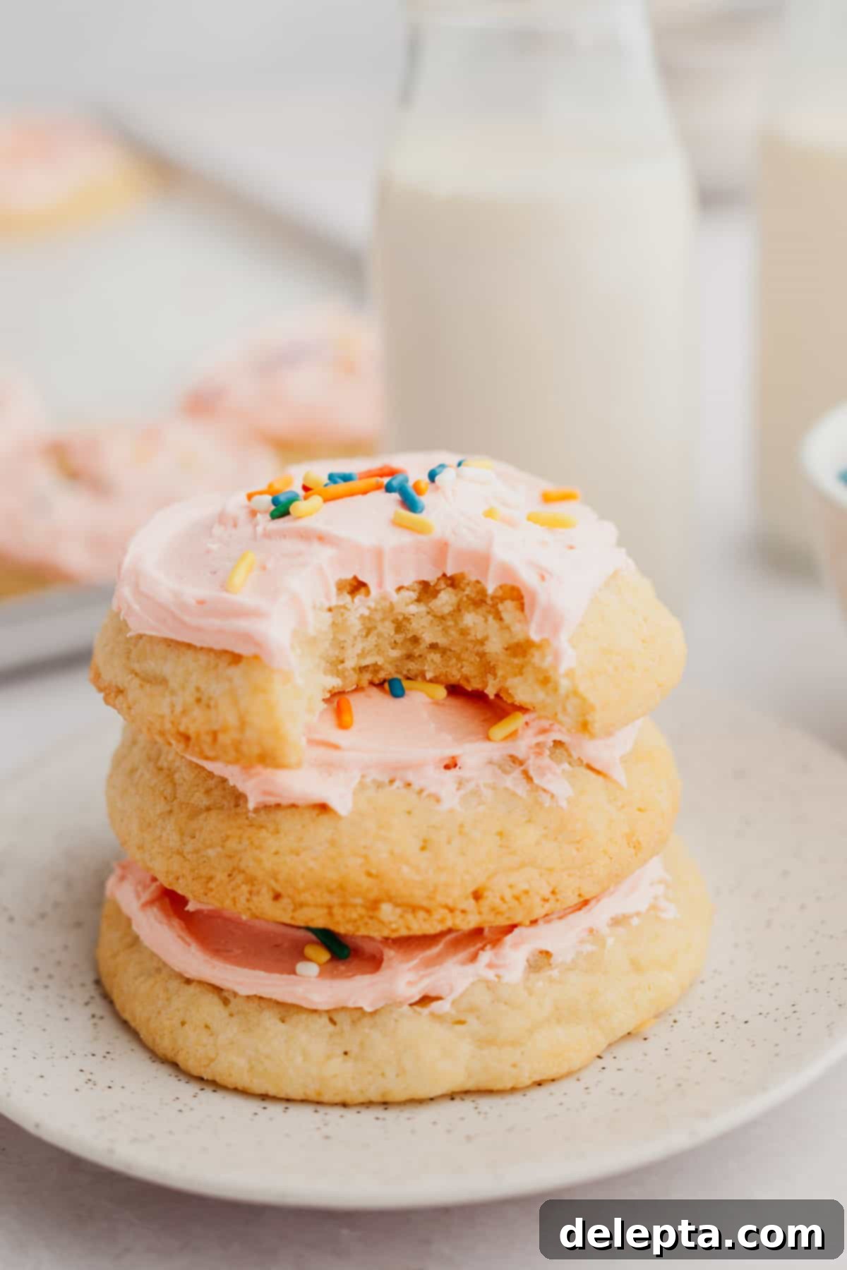 Velvet Buttercream Cookies 2 A stack of three soft pink frosted sugar cookies, generously covered in creamy frosting and sprinkles, resting on a white plate, inviting a nostalgic bite.