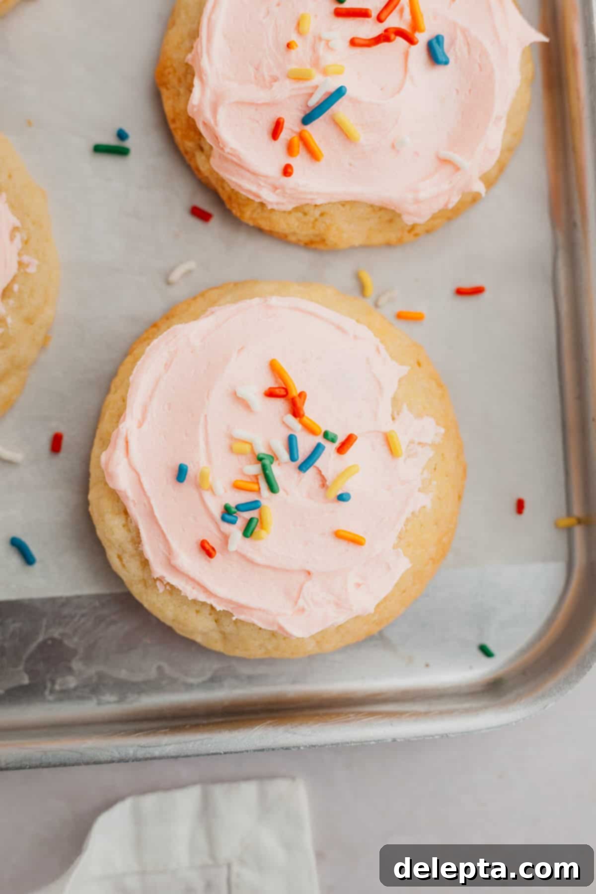 Velvet Buttercream Cookies 8 A baking tray filled with freshly baked and pink frosted sugar cookies, each adorned with colorful sprinkles, showcasing their soft, inviting appearance.