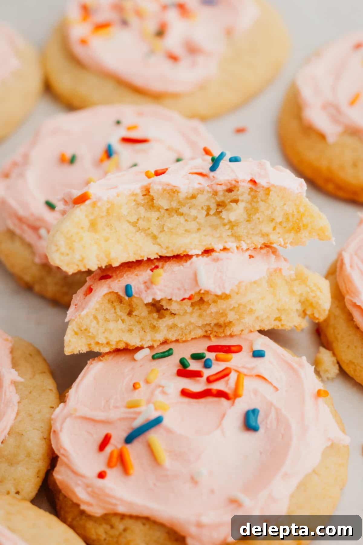 Velvet Buttercream Cookies 9 A close-up shot of several pink frosted sugar cookies, with one cookie cut in half to reveal its incredibly soft and tender interior, inviting a taste.