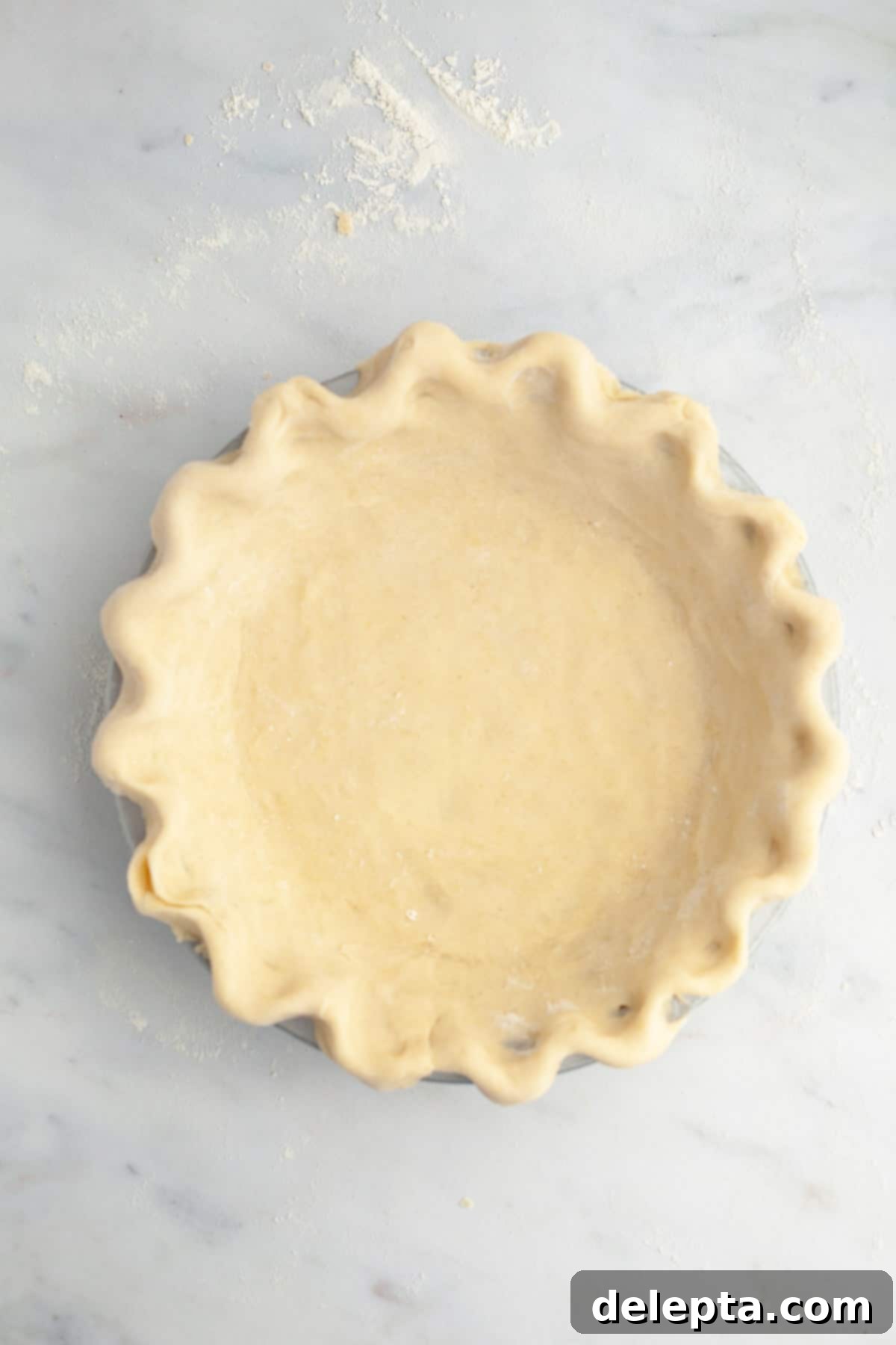 Perfectly Flaky Homemade Pie Crust 2 Crimped pie in a pie plate, unbaked, showcasing a perfectly formed crust ready for filling.