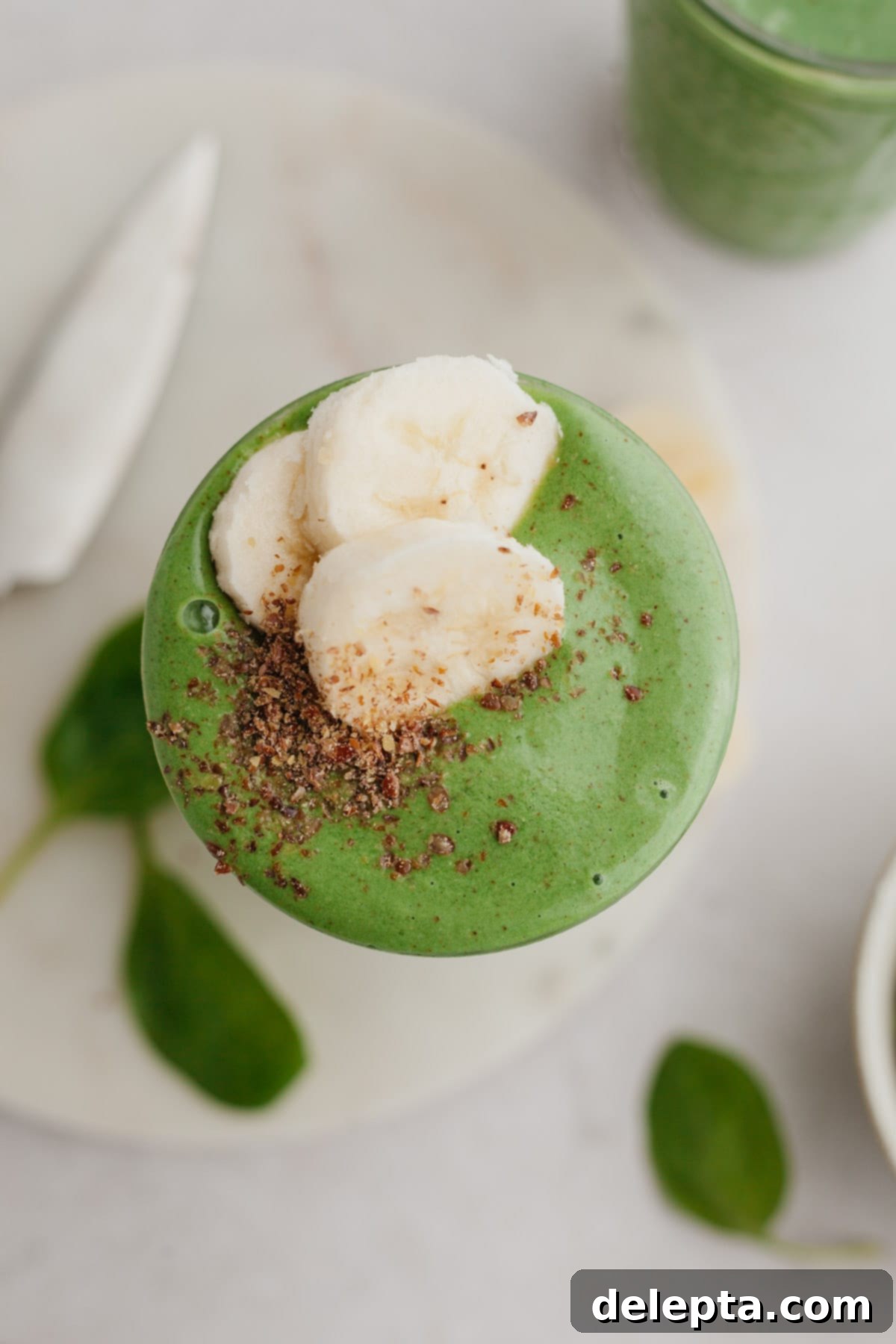 Green Velvet Revitalizer 5 An inviting overhead shot of a banana spinach smoothie, elegantly garnished with several slices of fresh banana.
