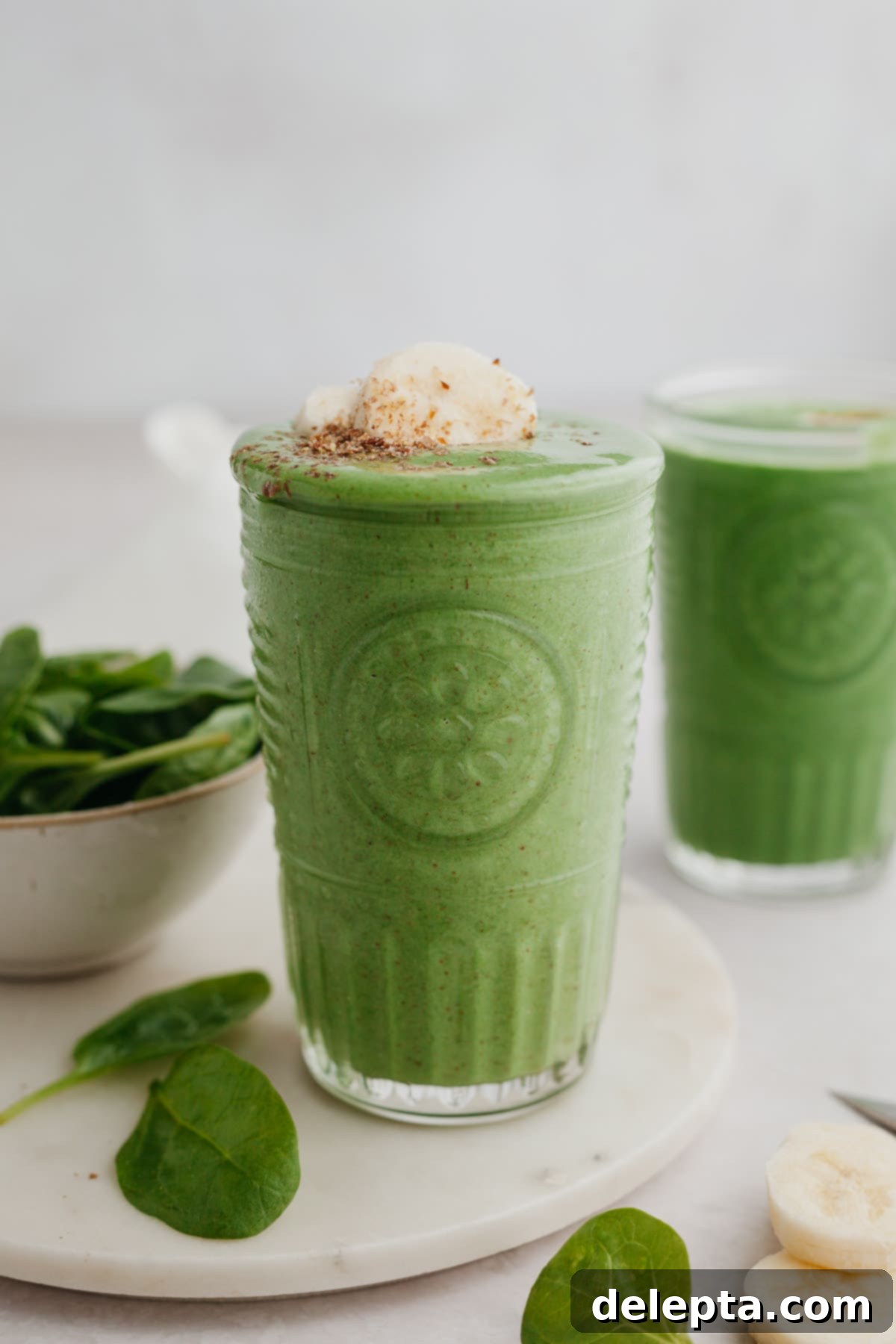 Green Velvet Revitalizer 6 A vibrant green banana spinach smoothie in a large glass, beautifully topped with slices of fresh banana.