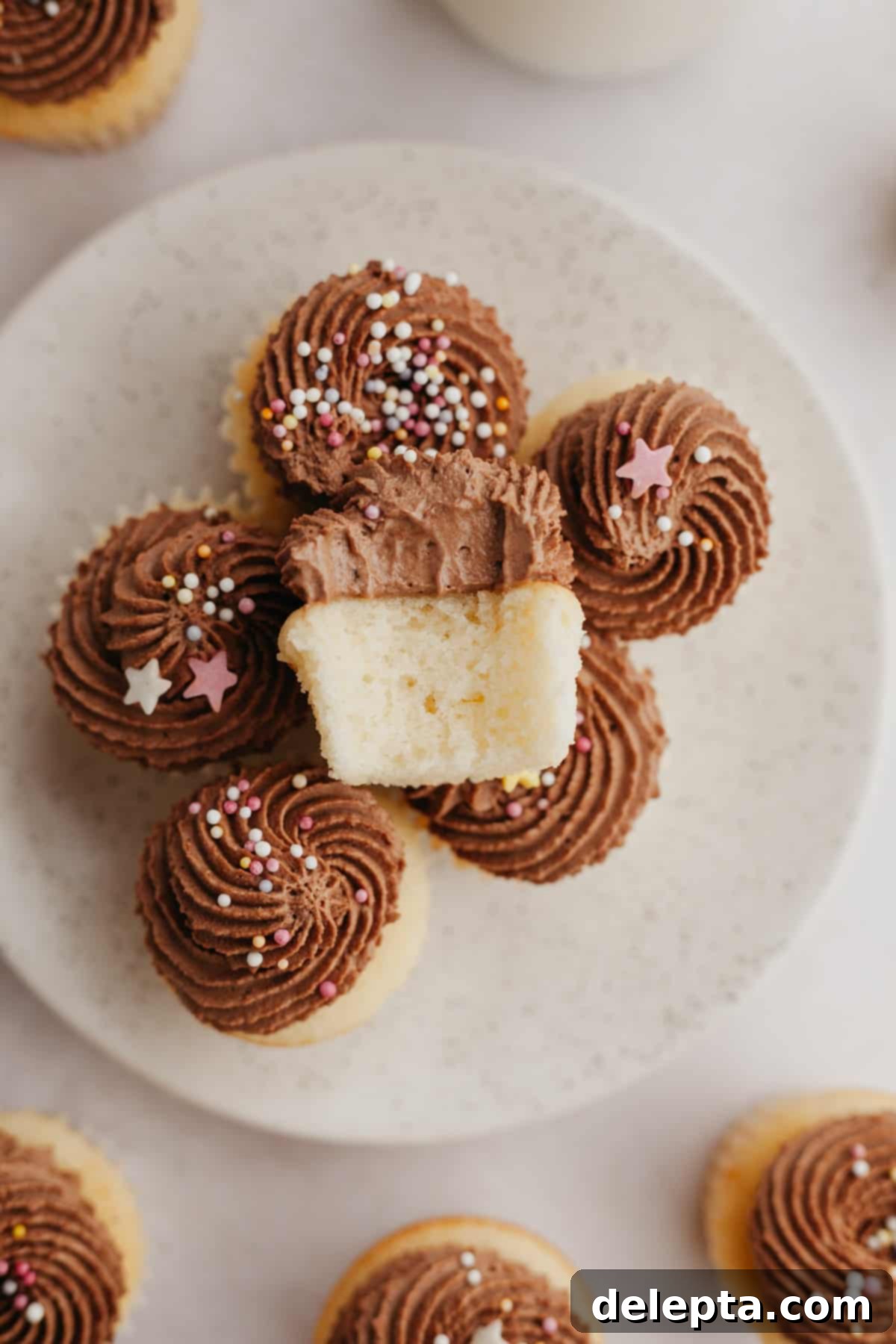 Dreamy Chocolate Cloud Frosting 2 A bunch of mini vanilla cupcakes with chocolate frosting on a plate, one cupcake is on top with a bite taken out of it.