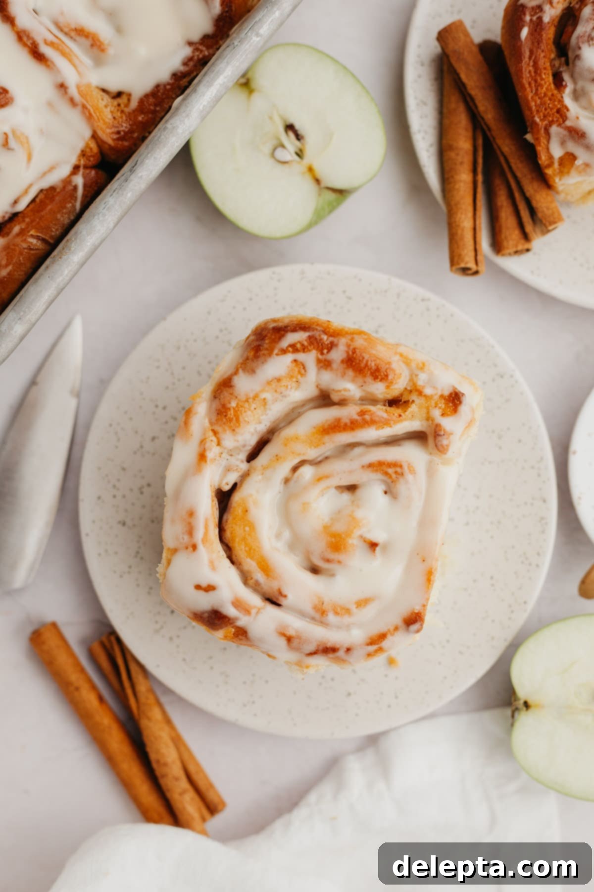 Apple Pie Stuffed Cinnamon Rolls 2 A cinnamon roll with apple pie filling on a small plate, generously topped with maple icing and a dusting of cinnamon.
