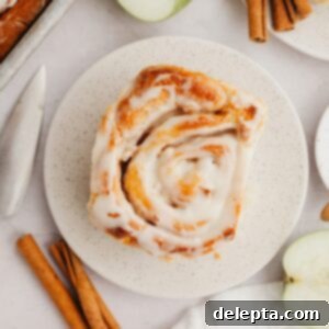 Apple Pie Stuffed Cinnamon Rolls 11 A cinnamon roll with apple pie filling on a small plate, generously topped with maple icing and a dusting of cinnamon.