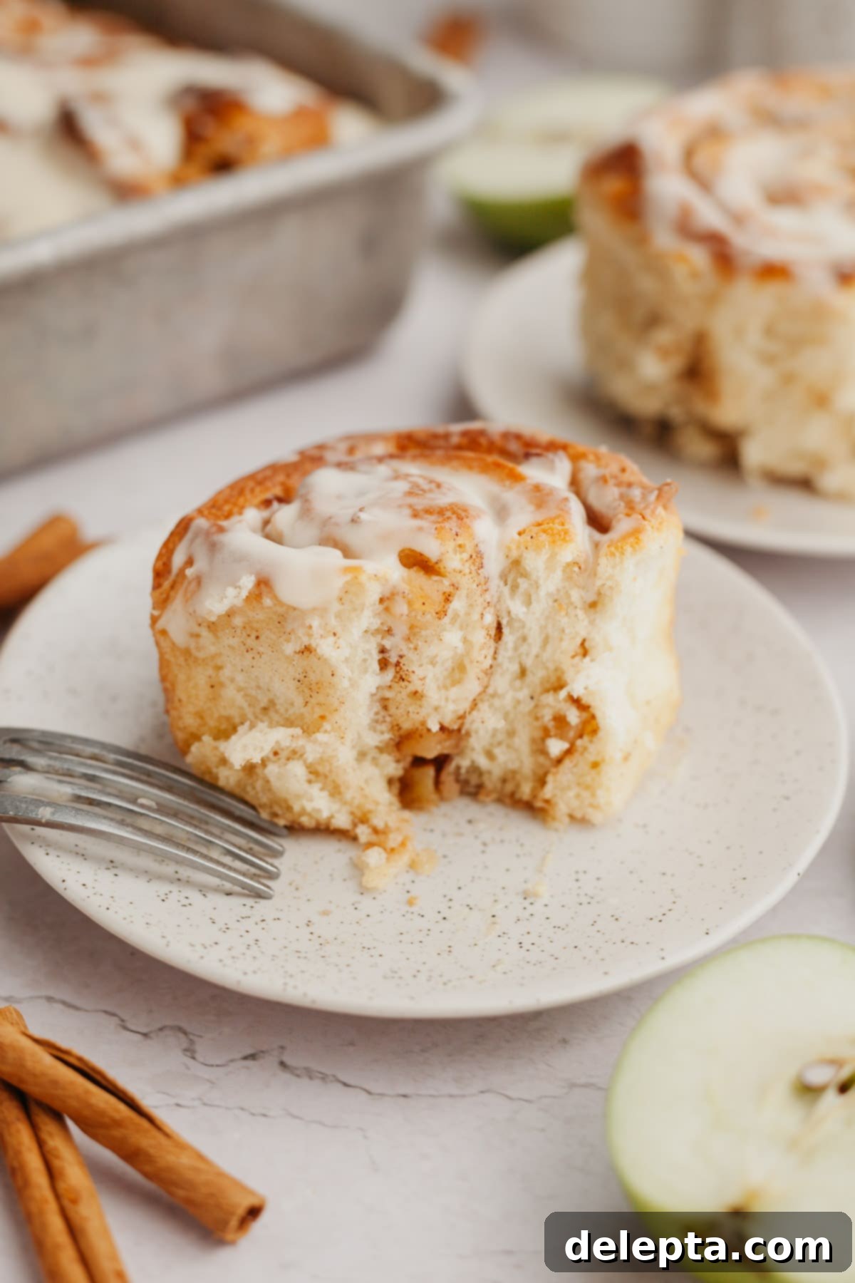Apple Pie Stuffed Cinnamon Rolls 10 A perfectly baked and iced cinnamon roll with apple pie filling on a small white plate, ready to be enjoyed.