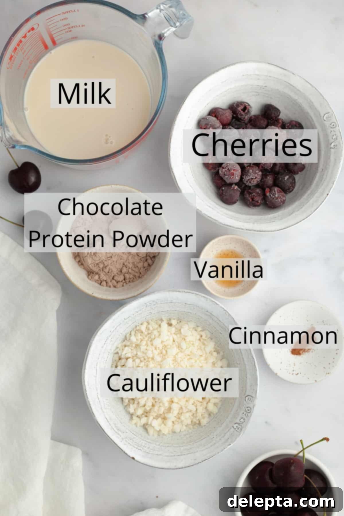 Speedy Chocolate Cherry Indulgence 3 A collection of measured ingredients neatly arranged in small bowls, including frozen cherries, cauliflower rice, milk, chocolate protein powder, cinnamon, and vanilla extract, ready to be blended into a chocolate cherry smoothie.