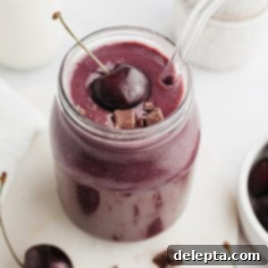 Speedy Chocolate Cherry Indulgence 6 A decadent chocolate cherry smoothie artfully presented in a glass jar, topped with a fresh, glossy cherry, inviting a delightful taste.