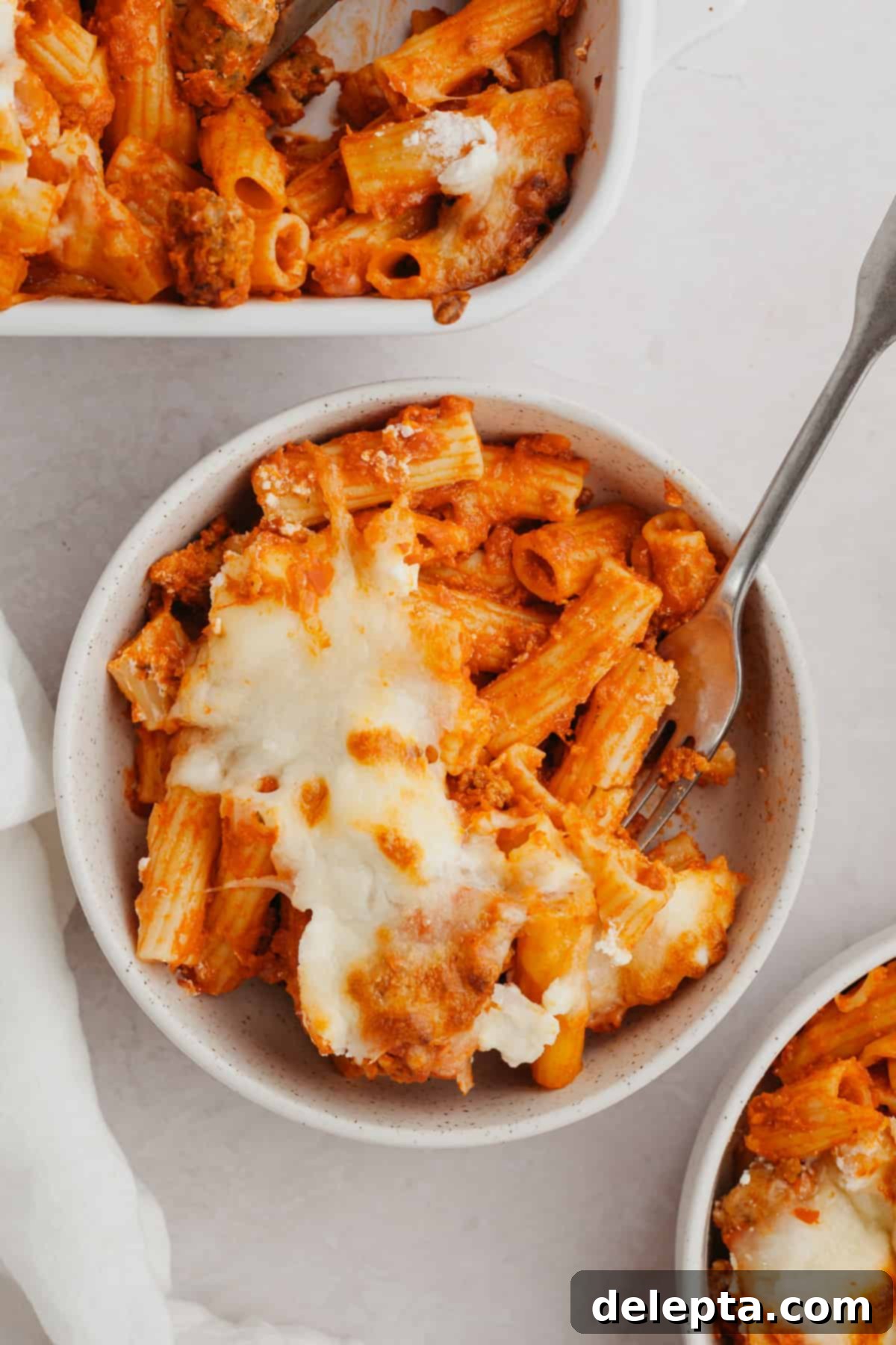 Hearty Three-Cheese Baked Rigatoni with Savory Sausage 8 A small white bowl filled with a serving of cheesy, baked orange pasta.