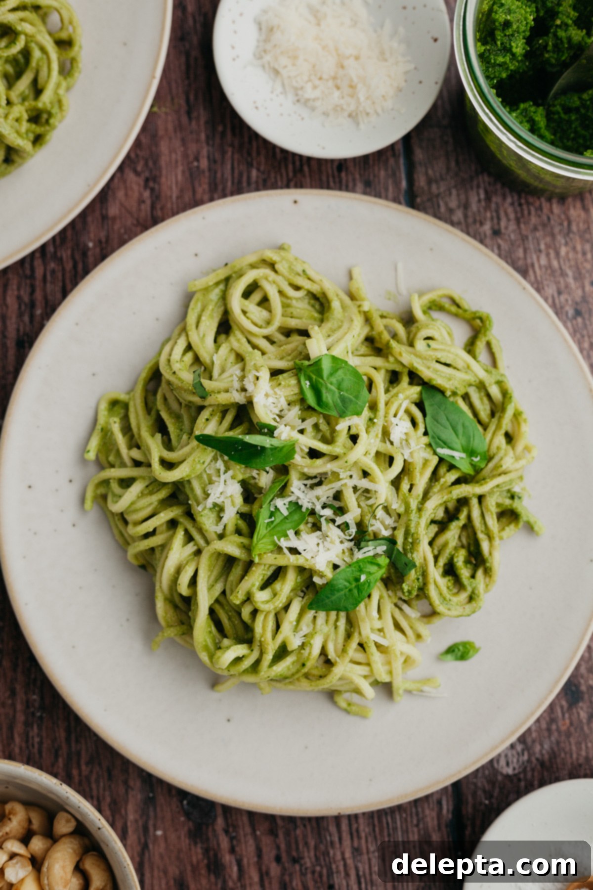 Homemade Pesto Pasta 2 A beautifully plated dish of pesto pasta on a large white plate, garnished with fresh basil leaves and grated Parmesan cheese.