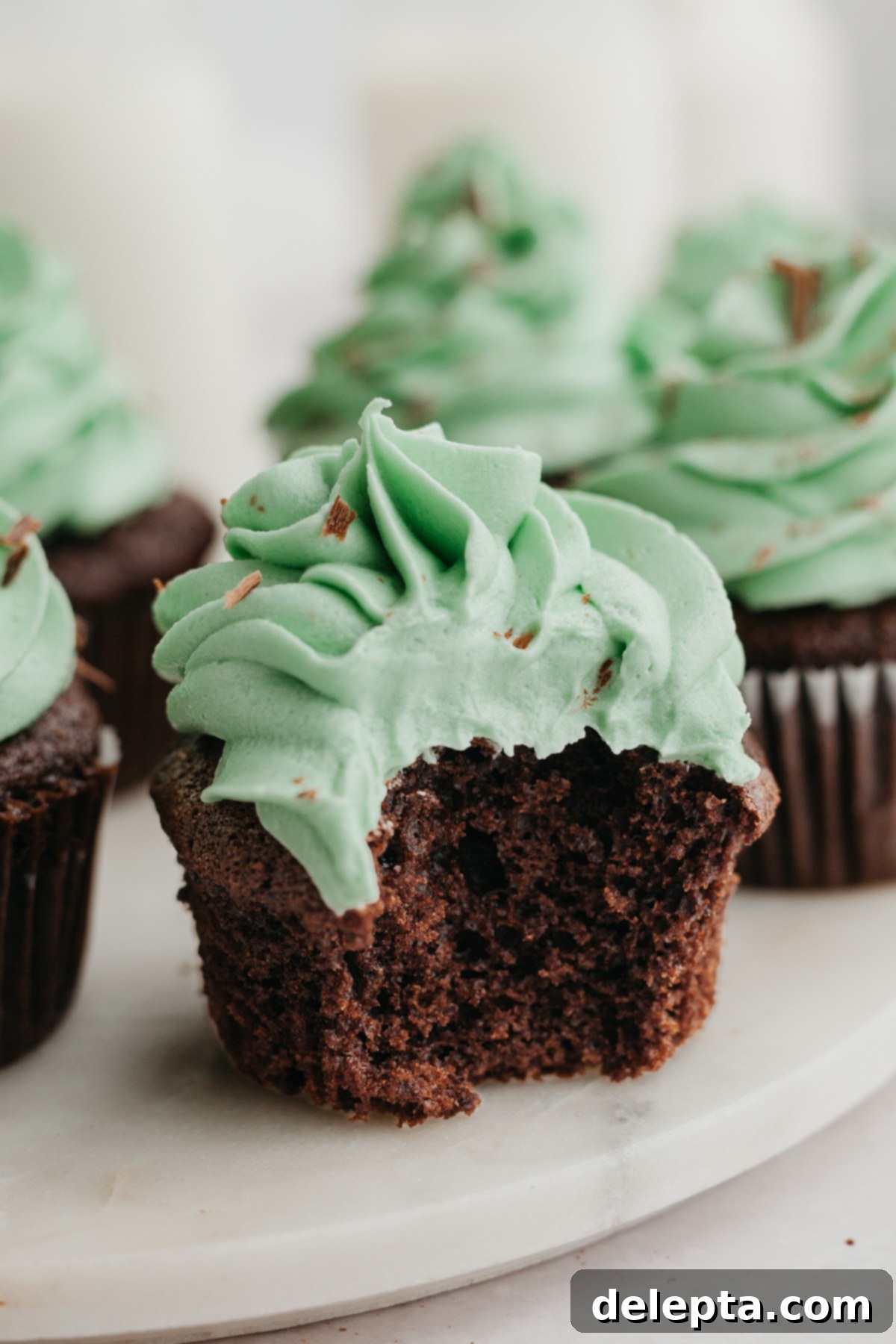 Effortless Five Minute Mint Frosting 6 A close-up of a chocolate cupcake with green mint frosting, a bite has been taken out of the cupcake, showing the soft interior.