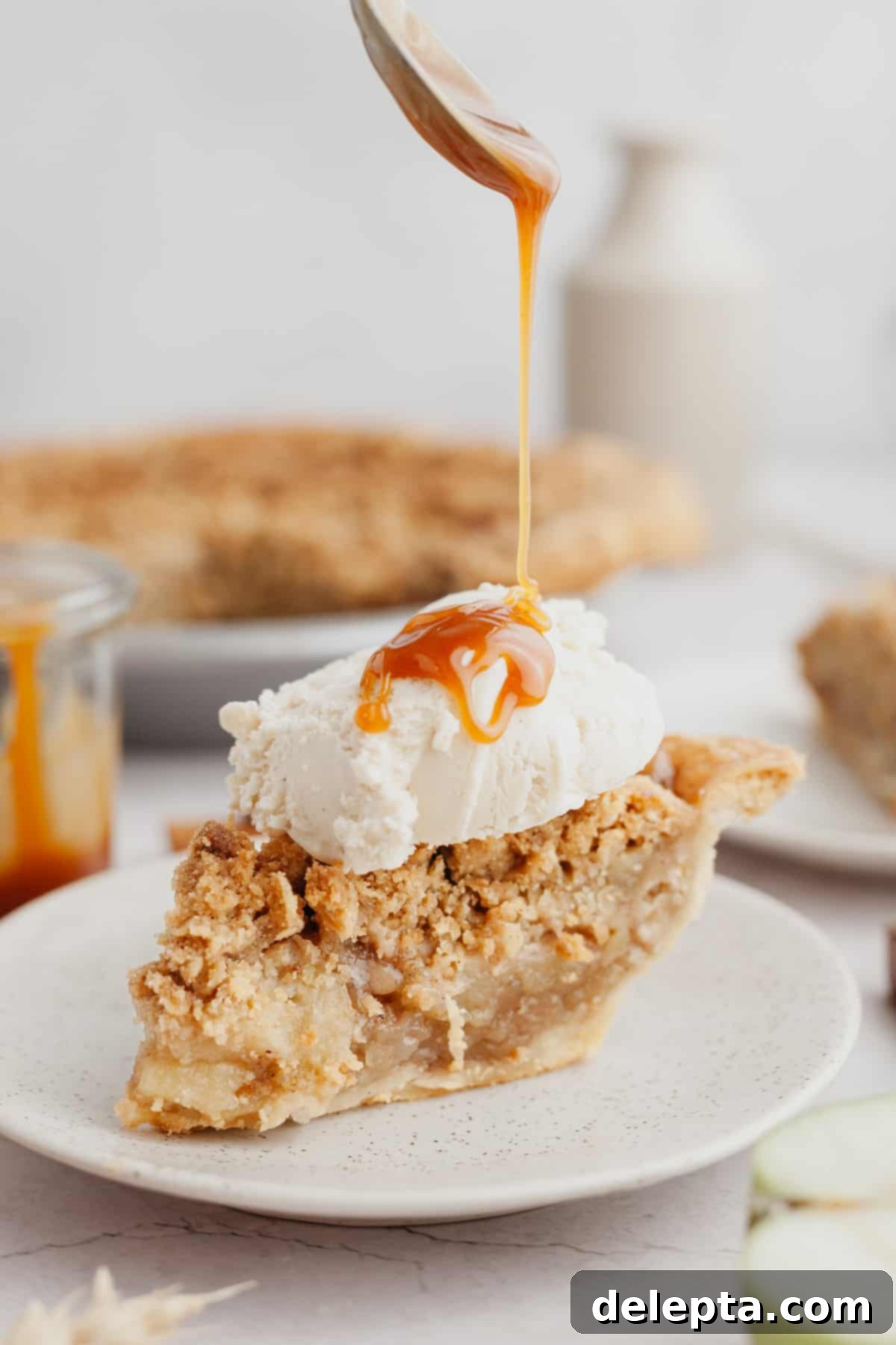 Rustic Oat Topped Apple Pie 2 A beautifully baked slice of apple oat crumble pie with a large scoop of melting vanilla ice cream and a swirl of caramel sauce on top.