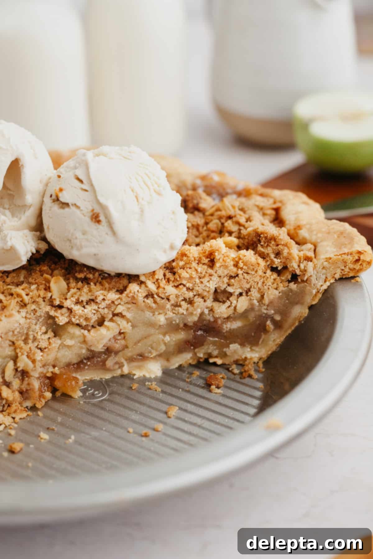 Rustic Oat Topped Apple Pie 7 A side view of a golden-brown apple oat crumble pie in a pie plate, topped with a generous scoop of vanilla ice cream.